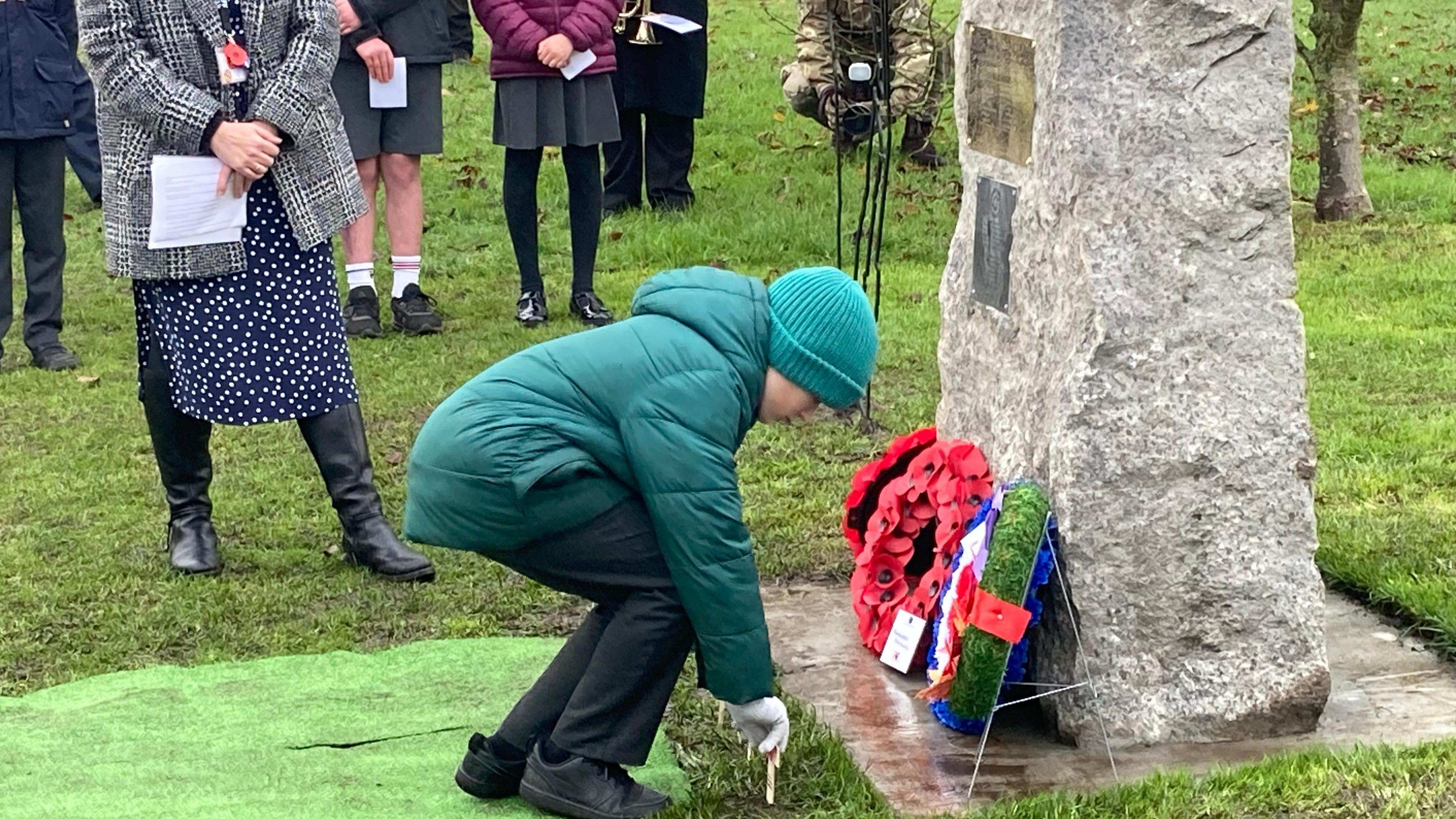 A pupil from Applegarth Primary School sets a cross in the ground in front of he memorial stone