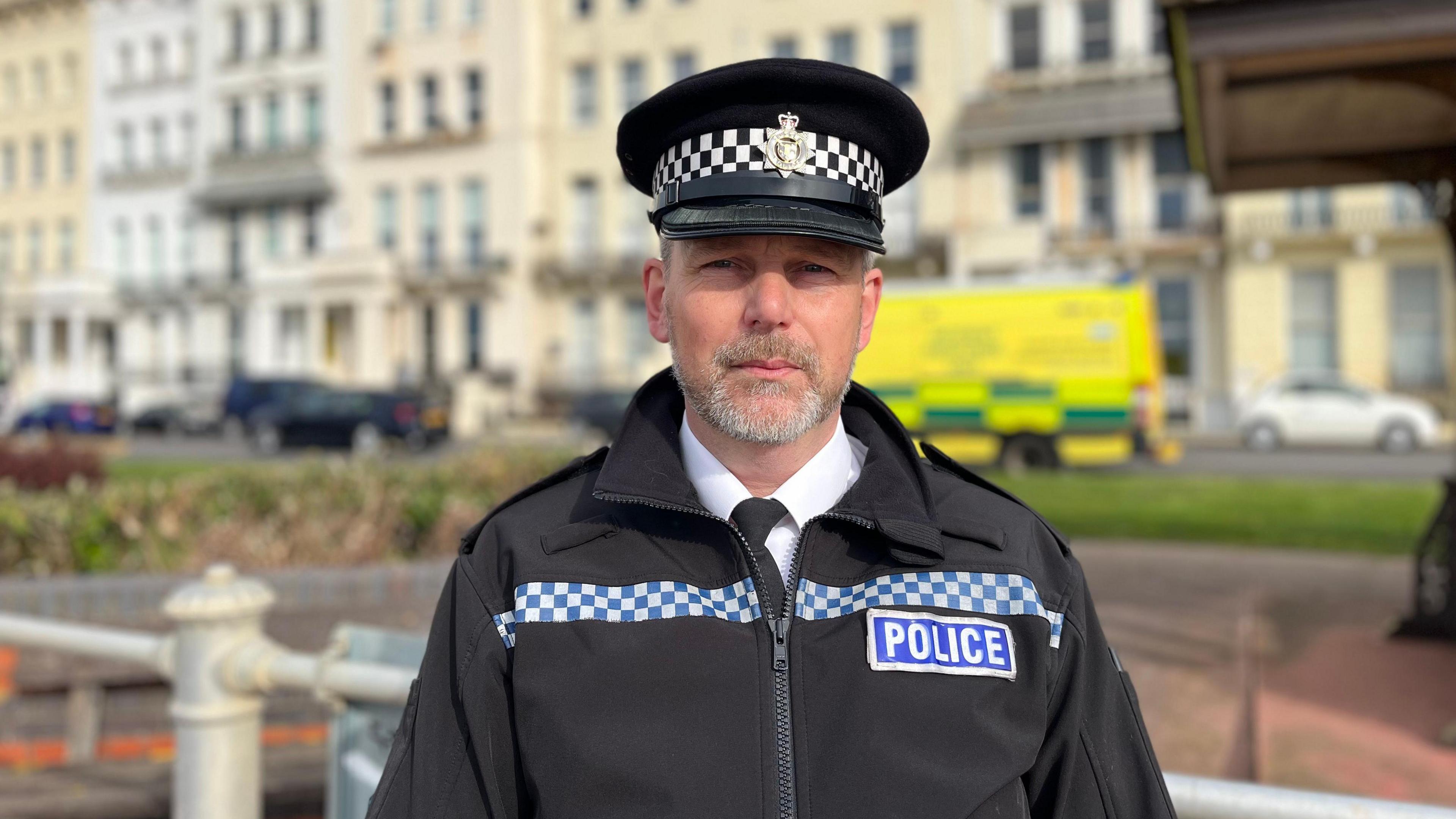 Sussex Police Chief Inspector James Scott in black police uniform with a black police hat, looking directly into the camera. 