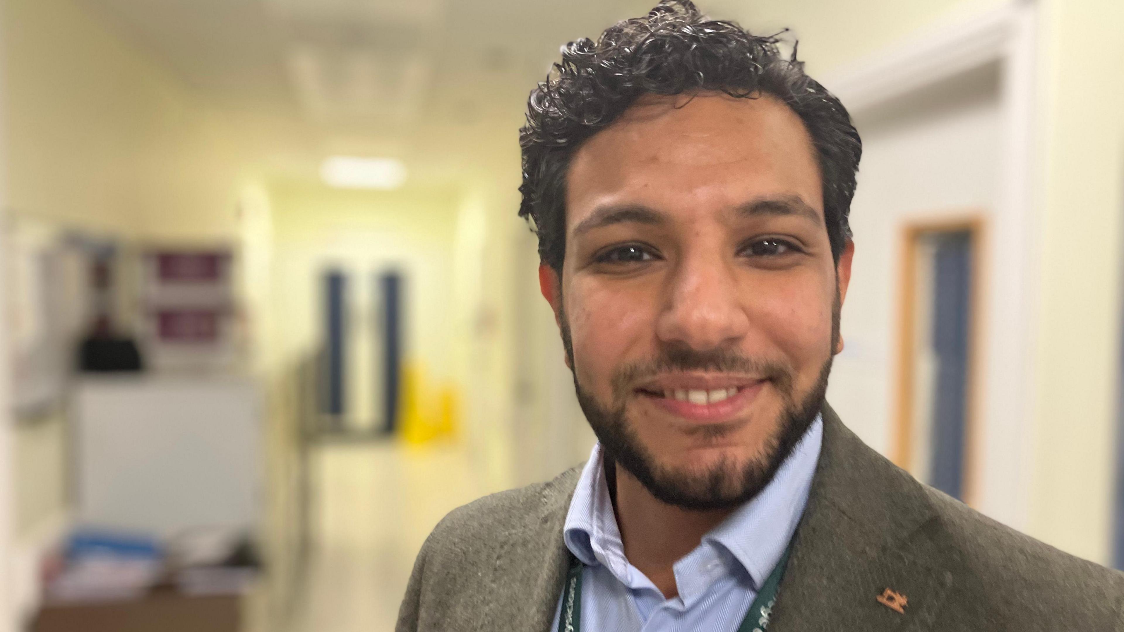 Dr Chirollos Romani smiles at the camera with a hospital corridor in the background.