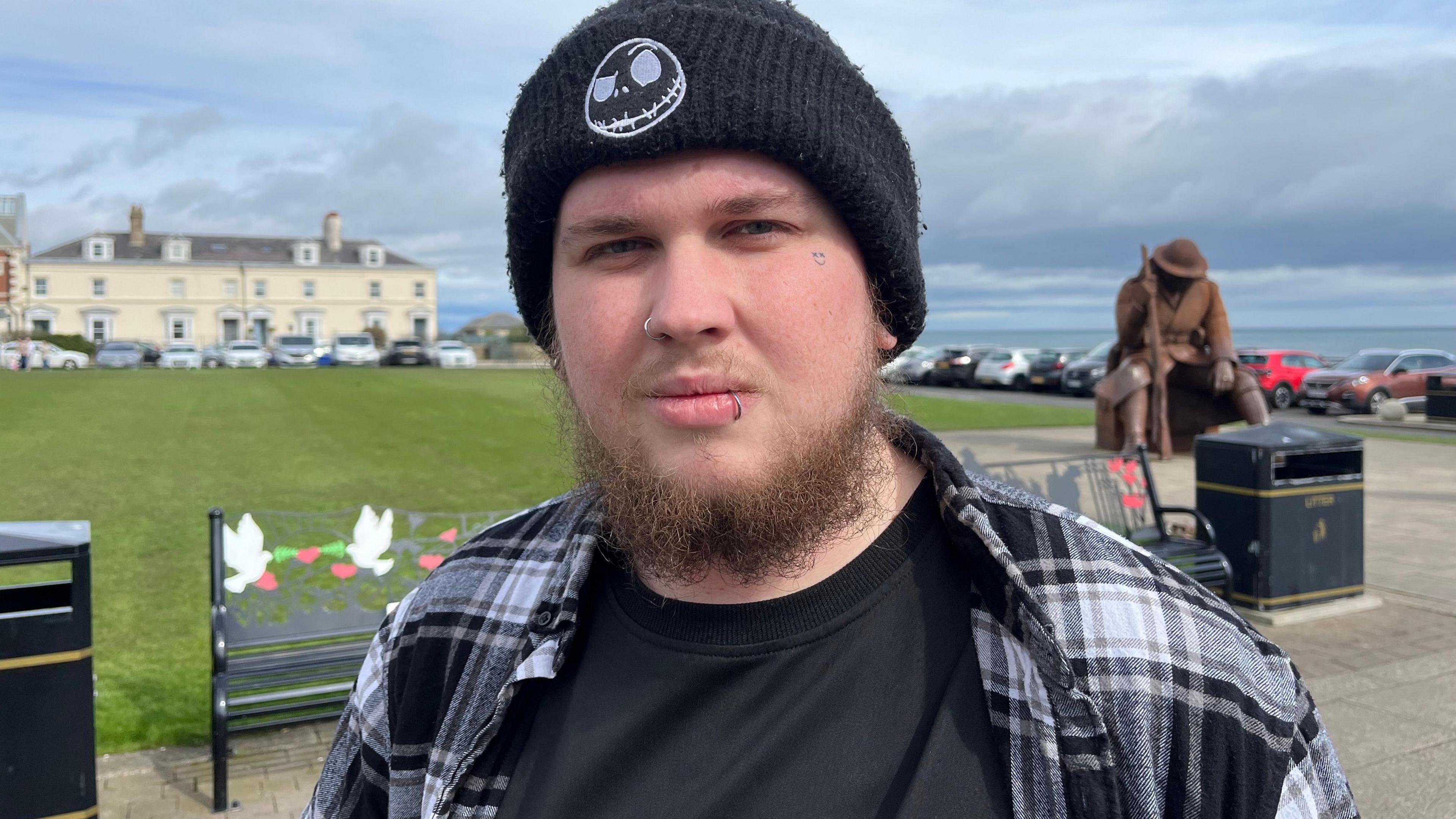 A young man with an earing in his lip standing in front of a row of cars at Seaham seafront