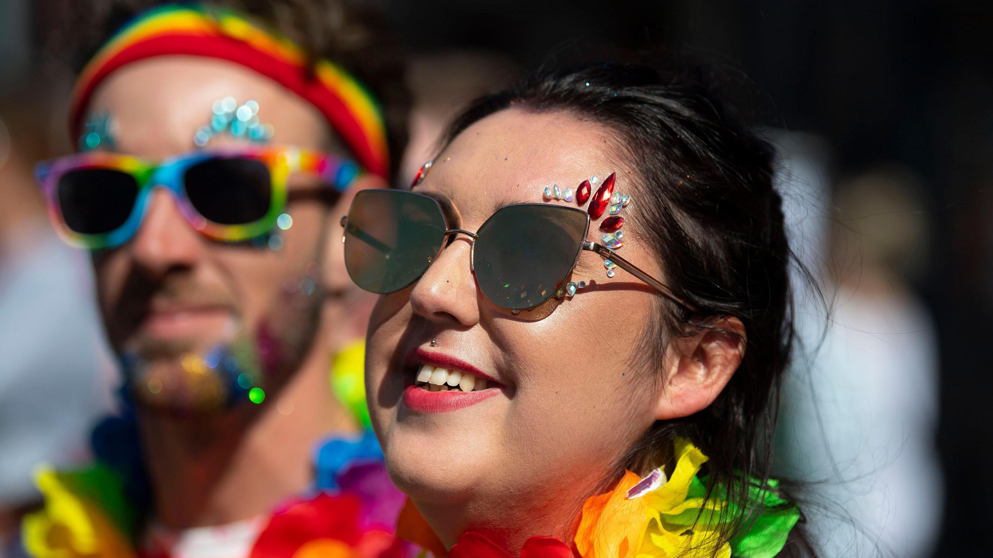 A young woman wearing LGBT coloured flowers around her neck.