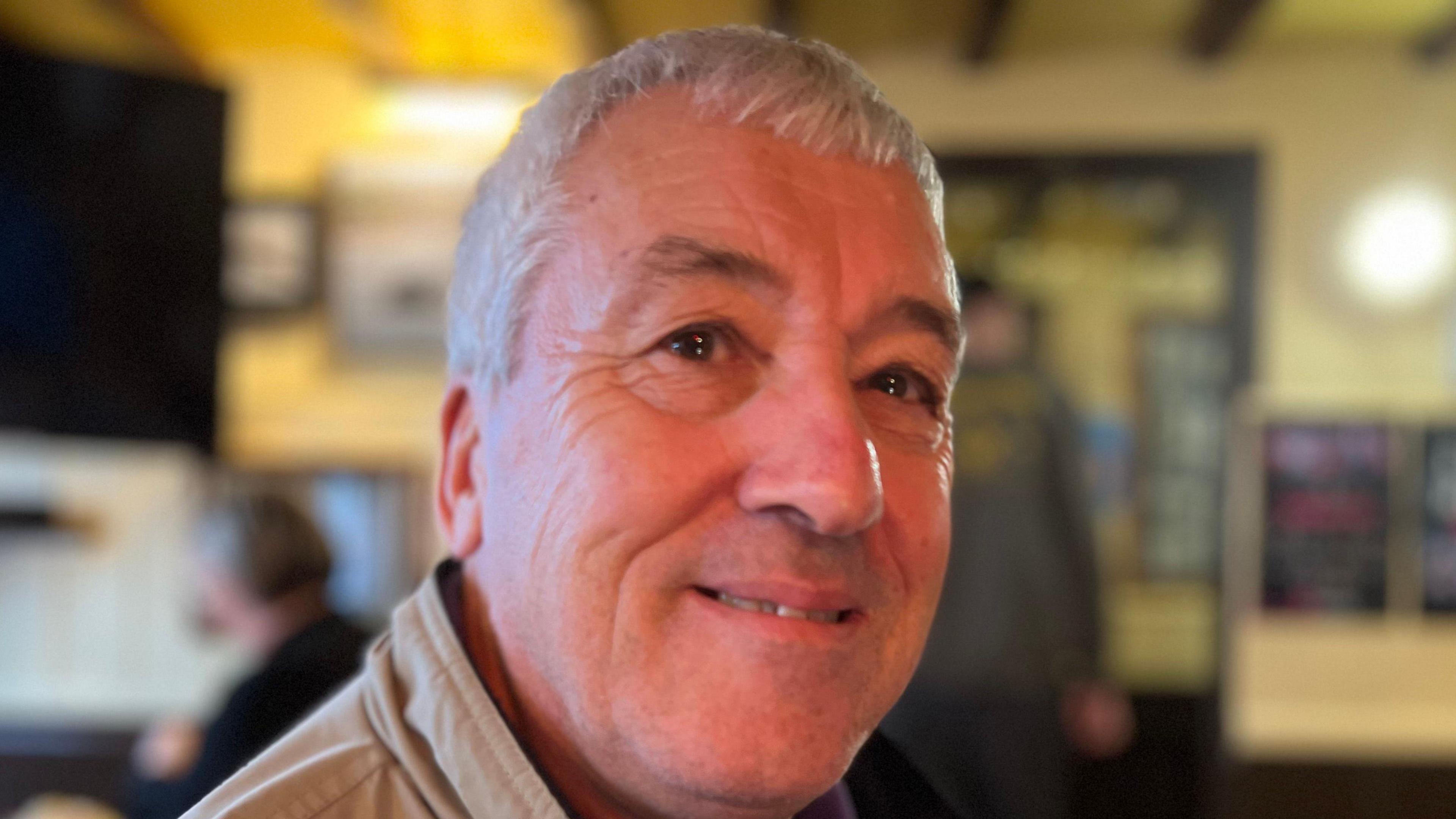 A older man with grey short hair wearing a Southampton football club jumper looking at the camera.