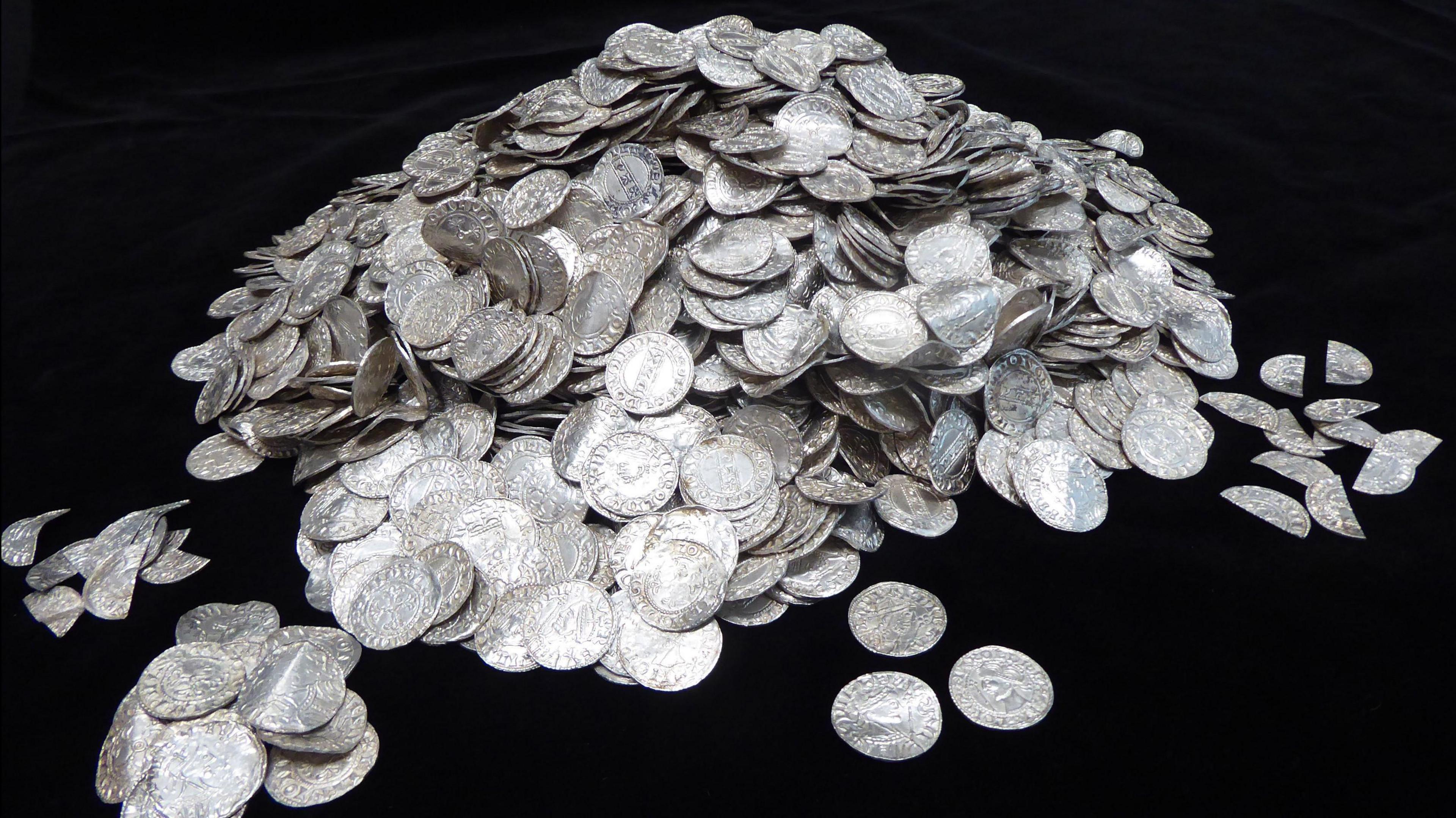 A hoard of silver coins in a pile which are pictured in front of a black backdrop.