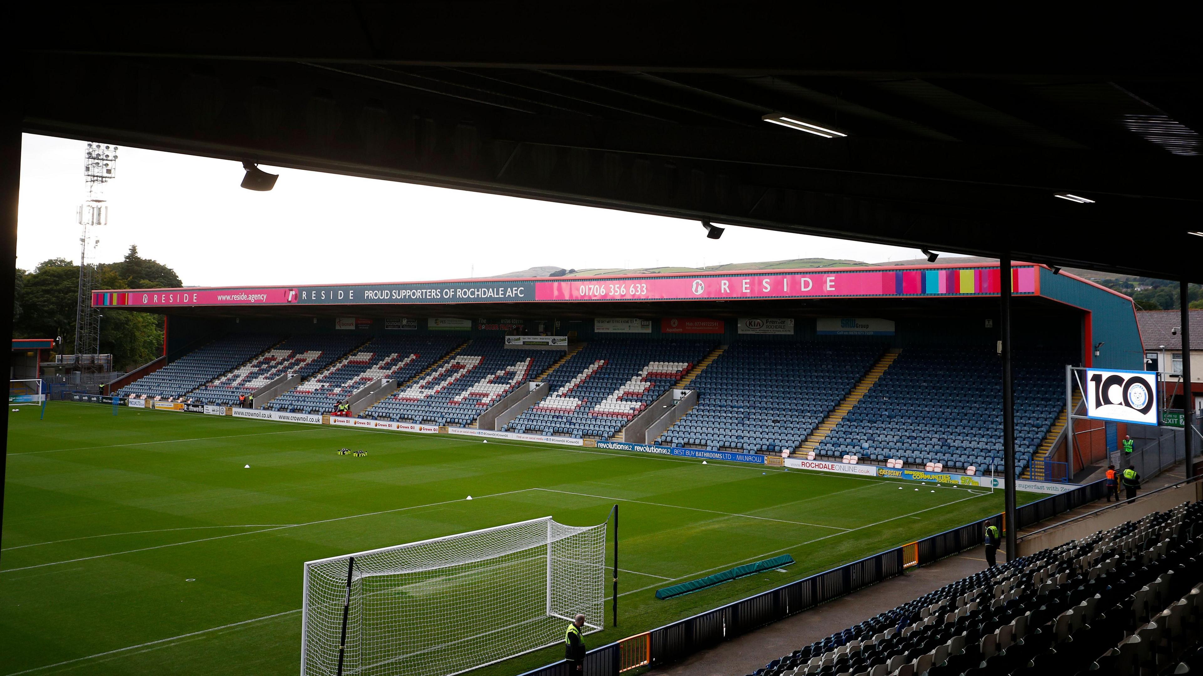 A view from behind the goal at Rochdale's Crown Oil Arena, with a view of the stand along the touchline with 'ROCHDALE' painted across the seats. 