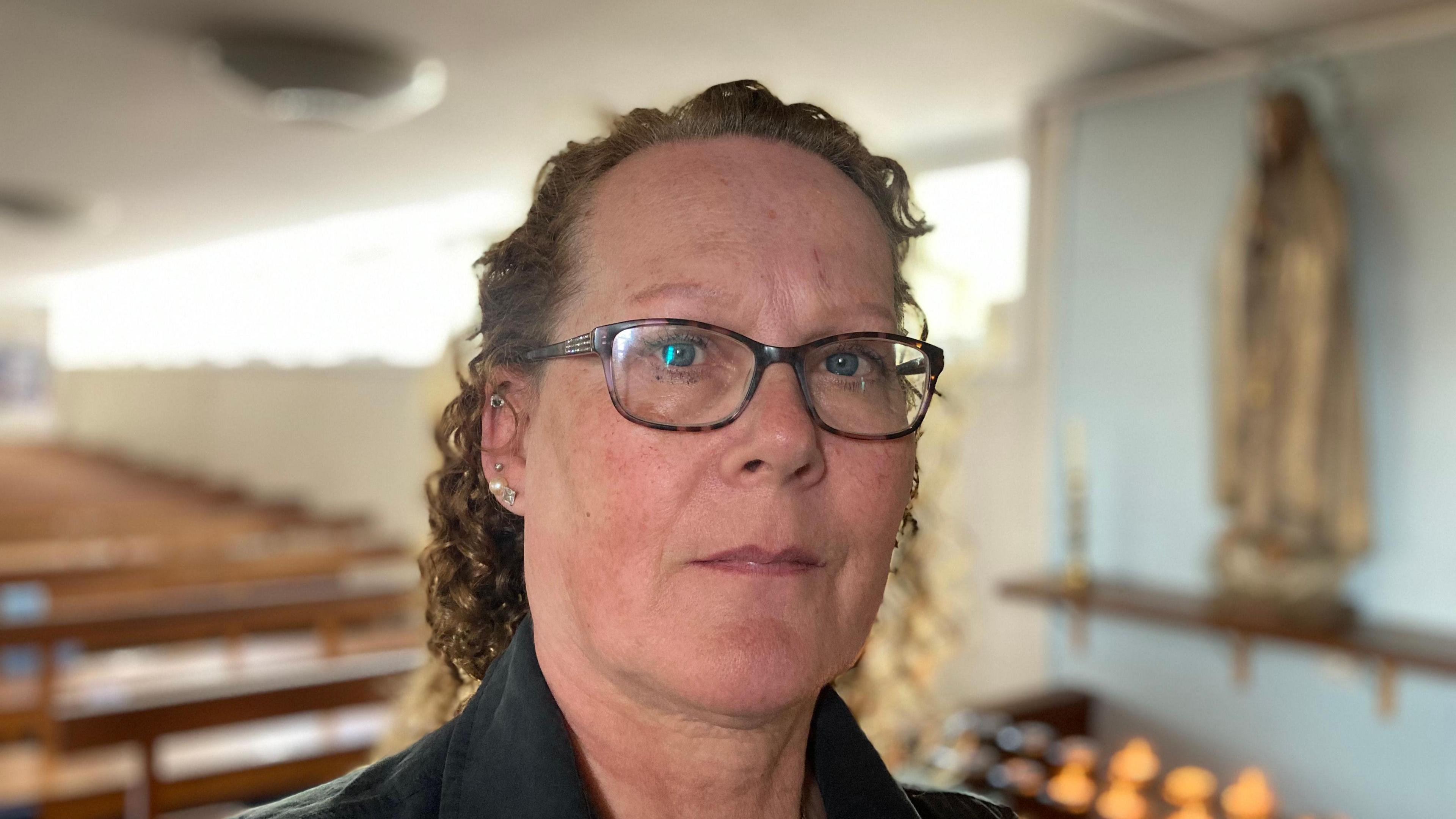 A close-up image of Maria Quinlan - a woman wearing glasses who is staring into the camera.