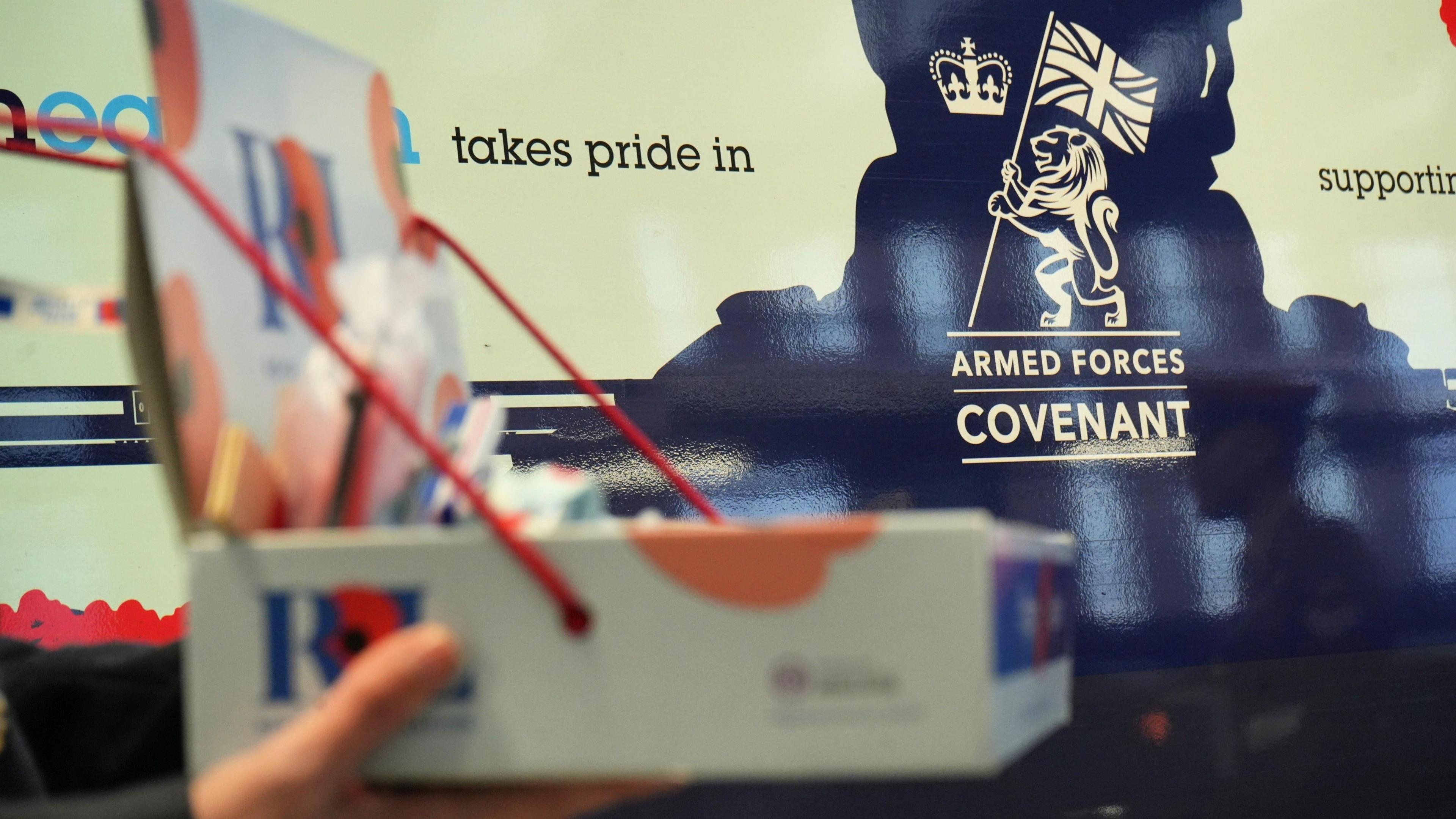 A hand holds a collecting tray for the Royal British Legion Poppy Appeal, with the image of the train in the background slightly blurred.
