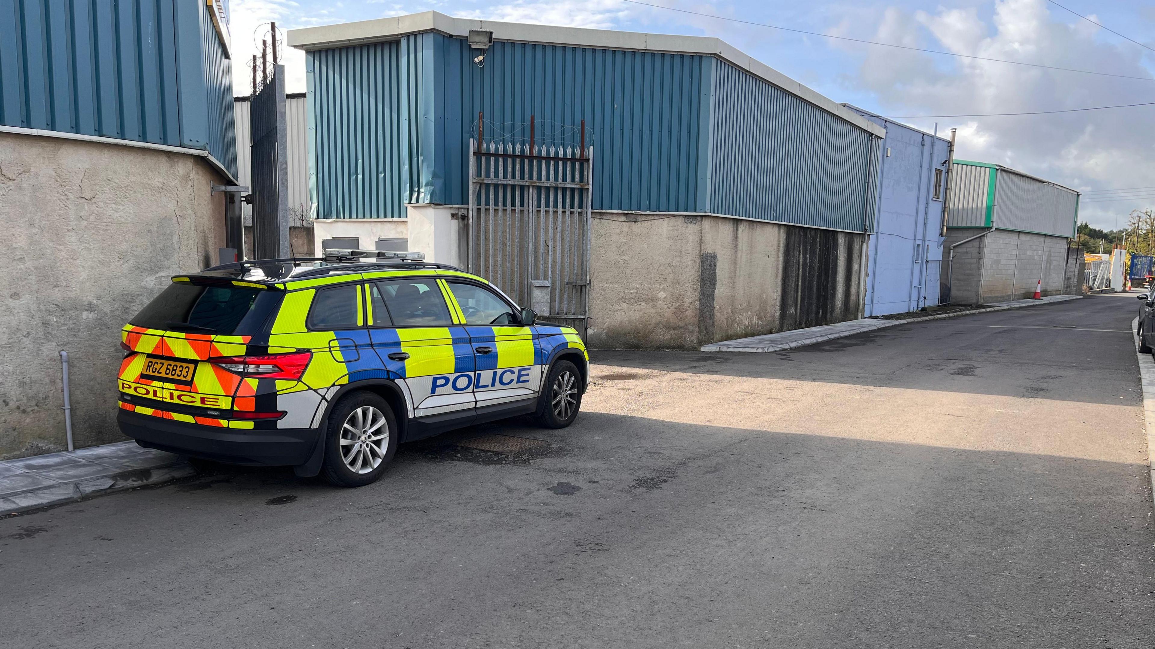 The back of a warehouse. A police car is parked