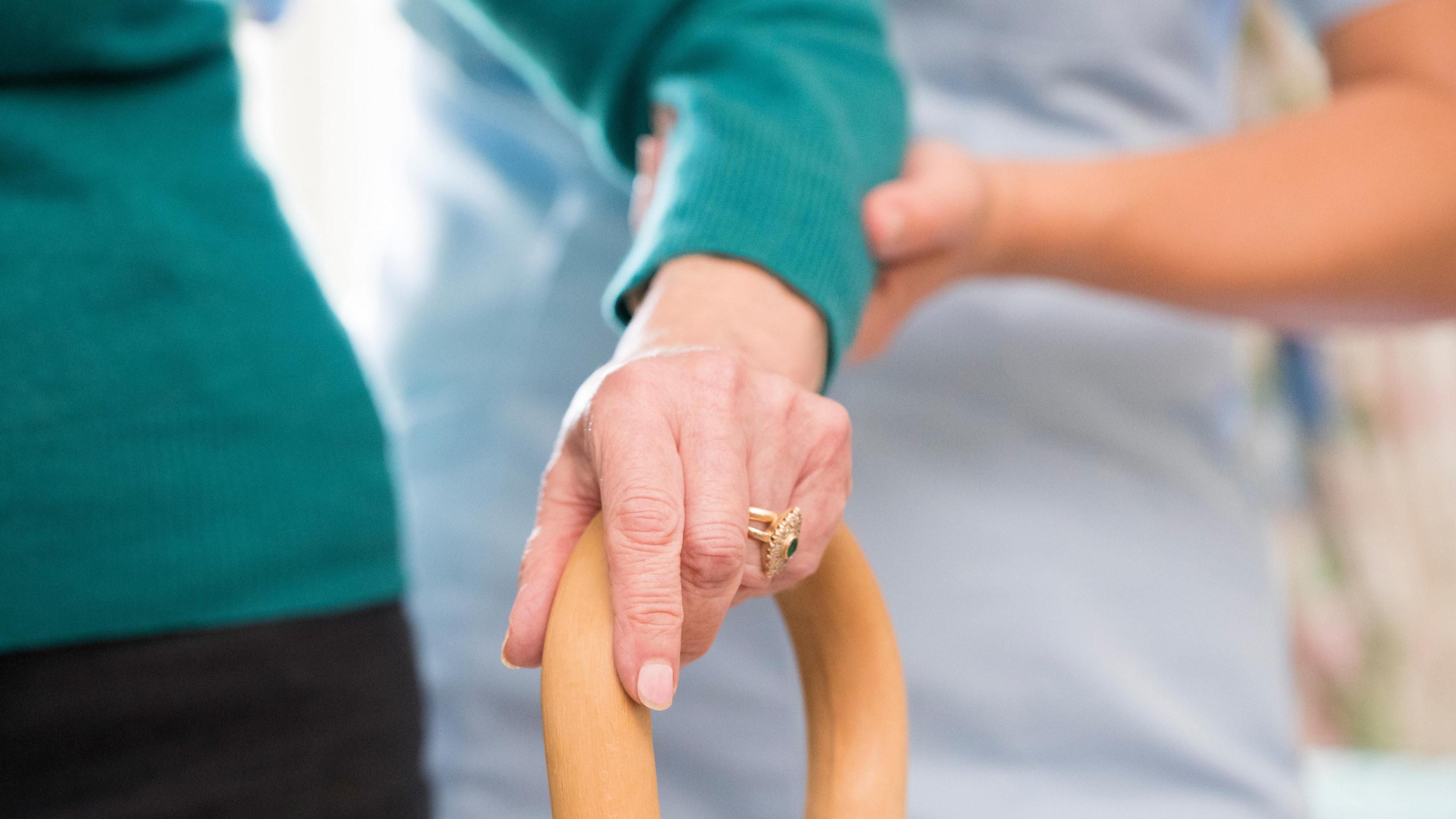 A female nurse helps support a senior person to walk with a walking stick. 