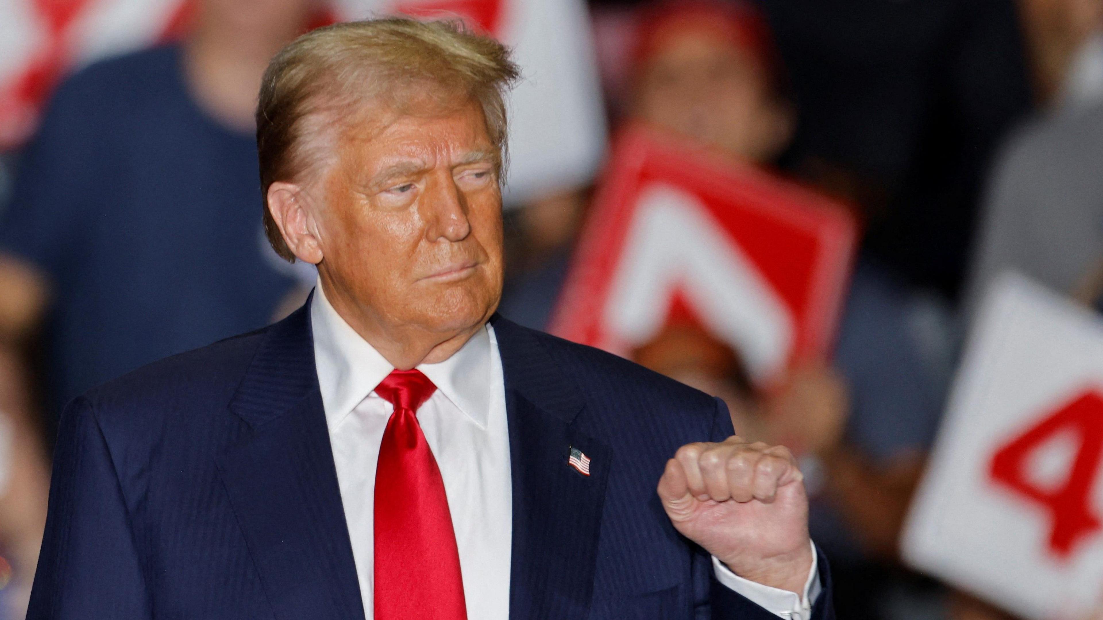 Trump stands at rally in Greensboro, NC with his fist up and several poeple in a blurred background holding ''47'' signs