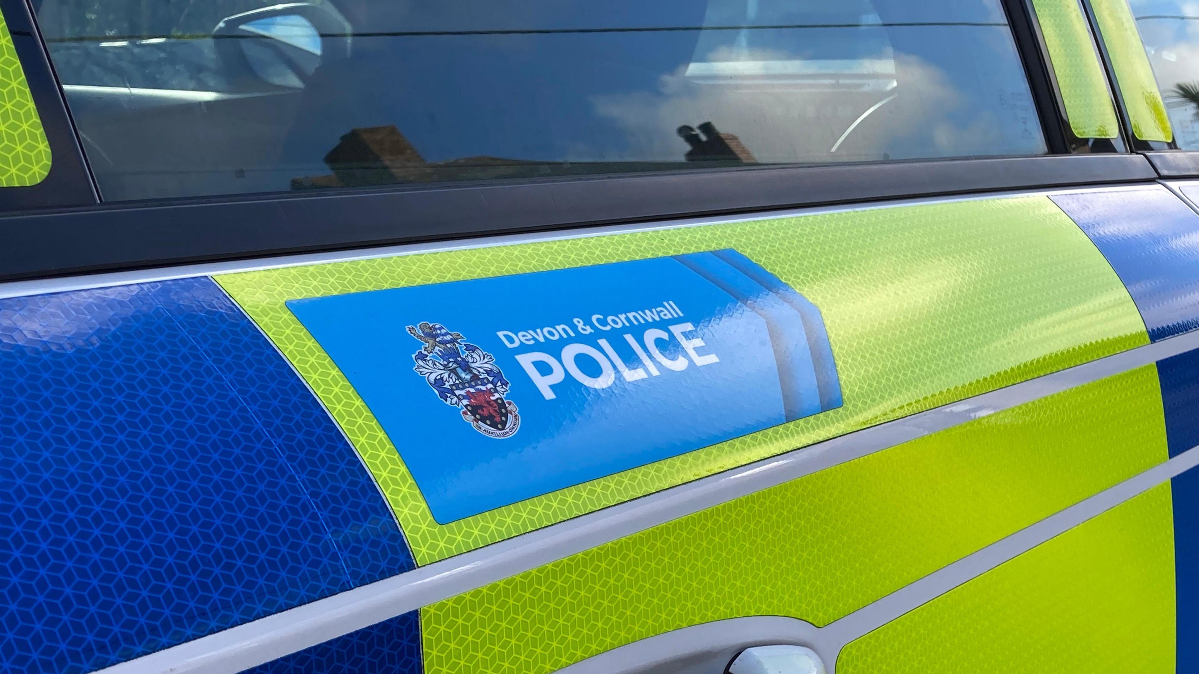 A picture of the side of the Devon and Cornwall police vehicle. It is green and blue in colour and has the forces blue logo on the side.