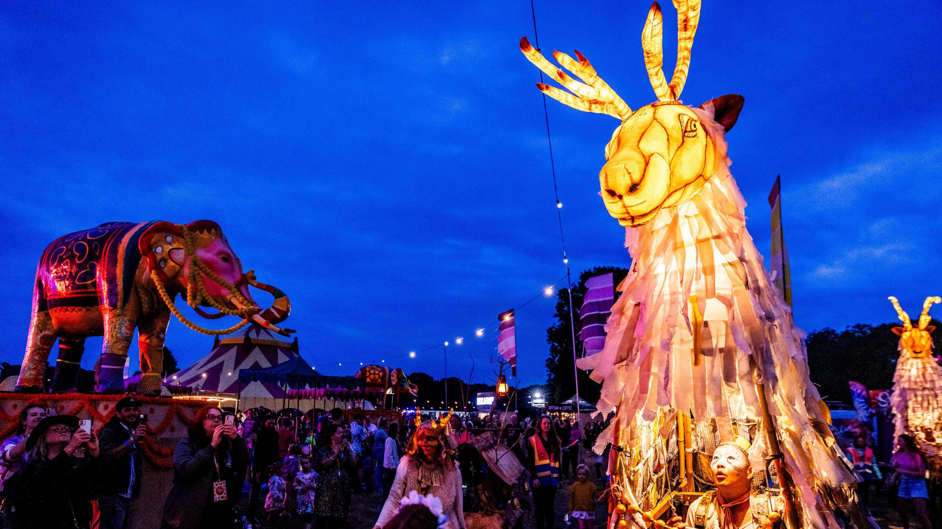 A lit-up model of a caribou in the foreground among the crowd at Camp Bestival 