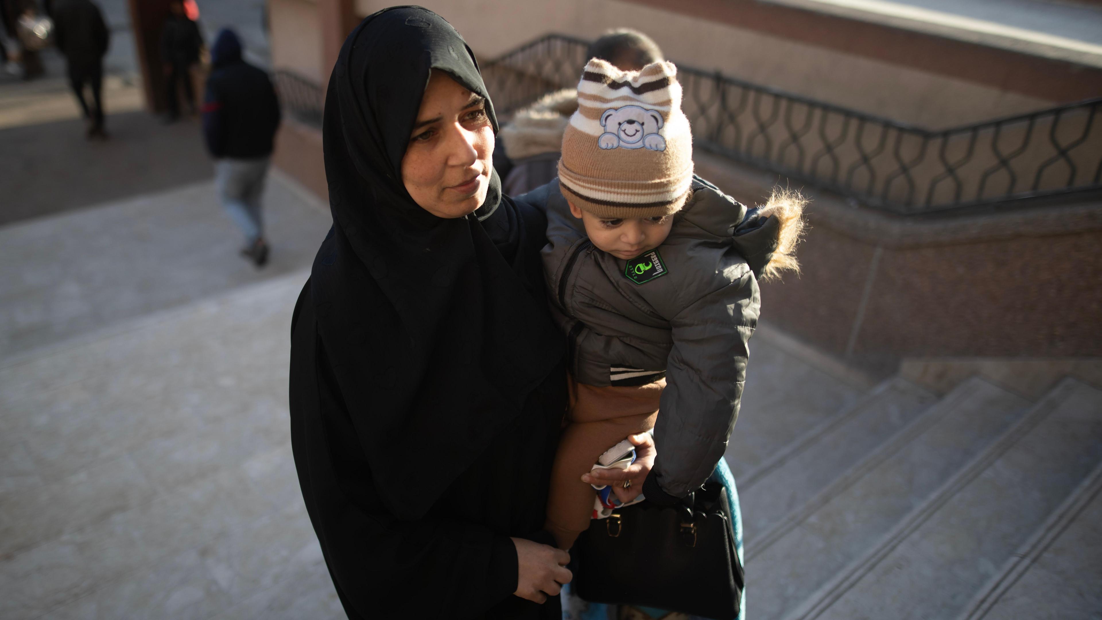 A Palestinian woman wearing a black abaya carrying a child walks up the stairs. 