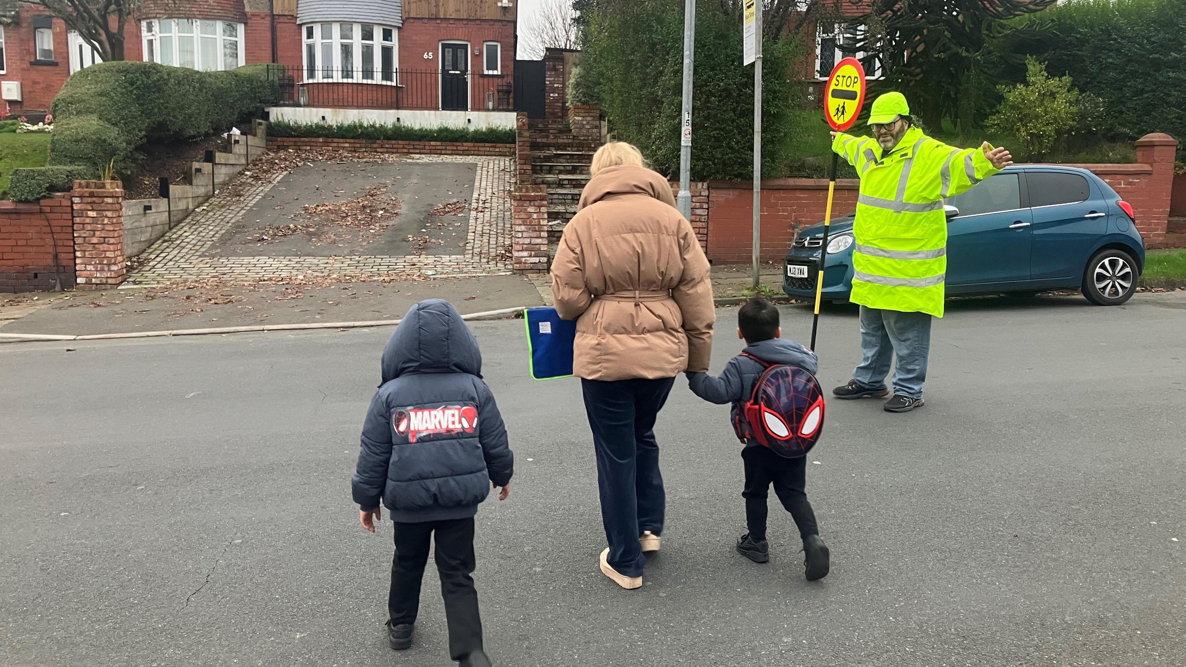 Lollipop man Barry Jones helping a family cross the road in Heywood