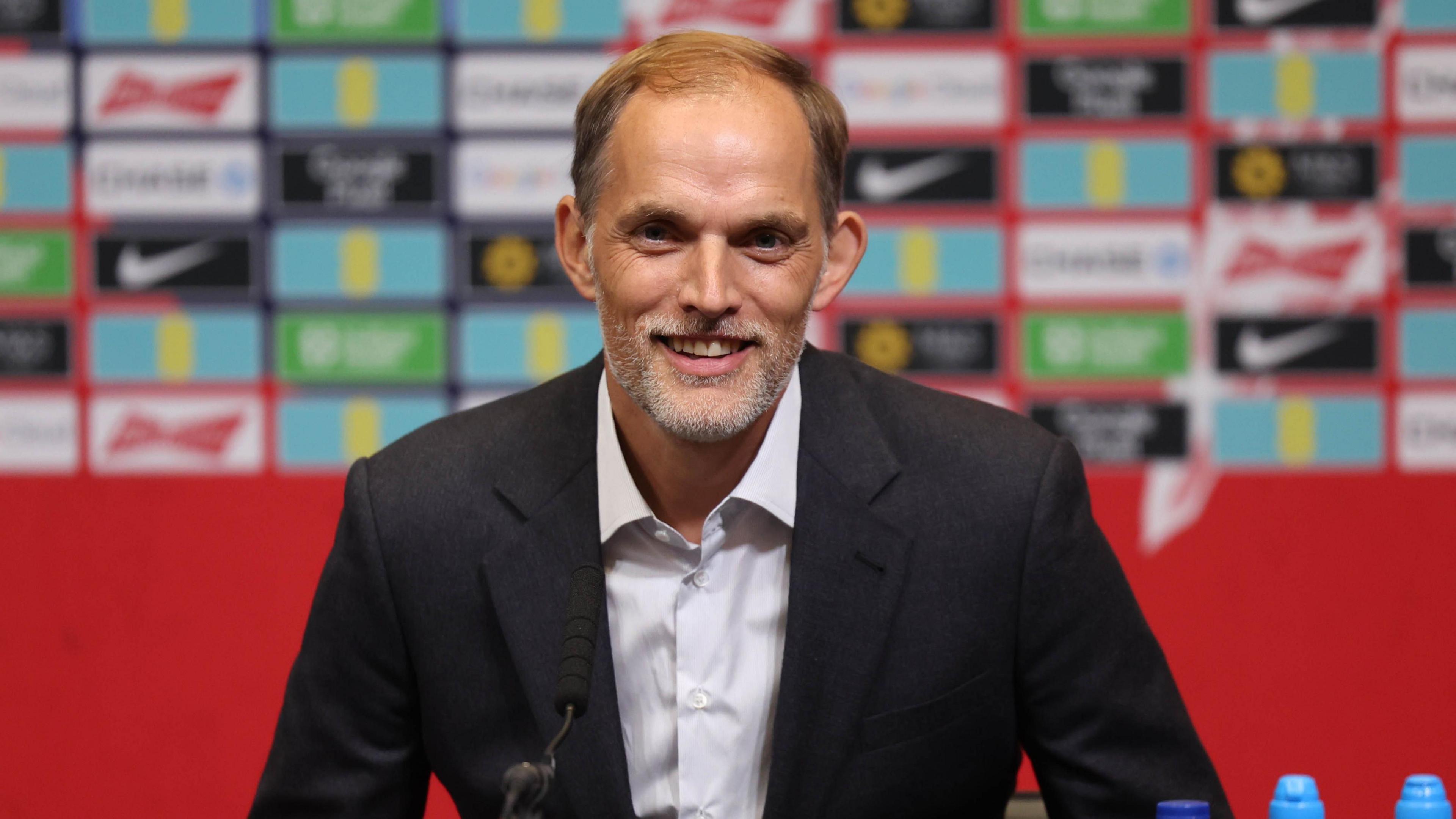 A man, Thomas Tuchel, sits at a press conference wearing a suit