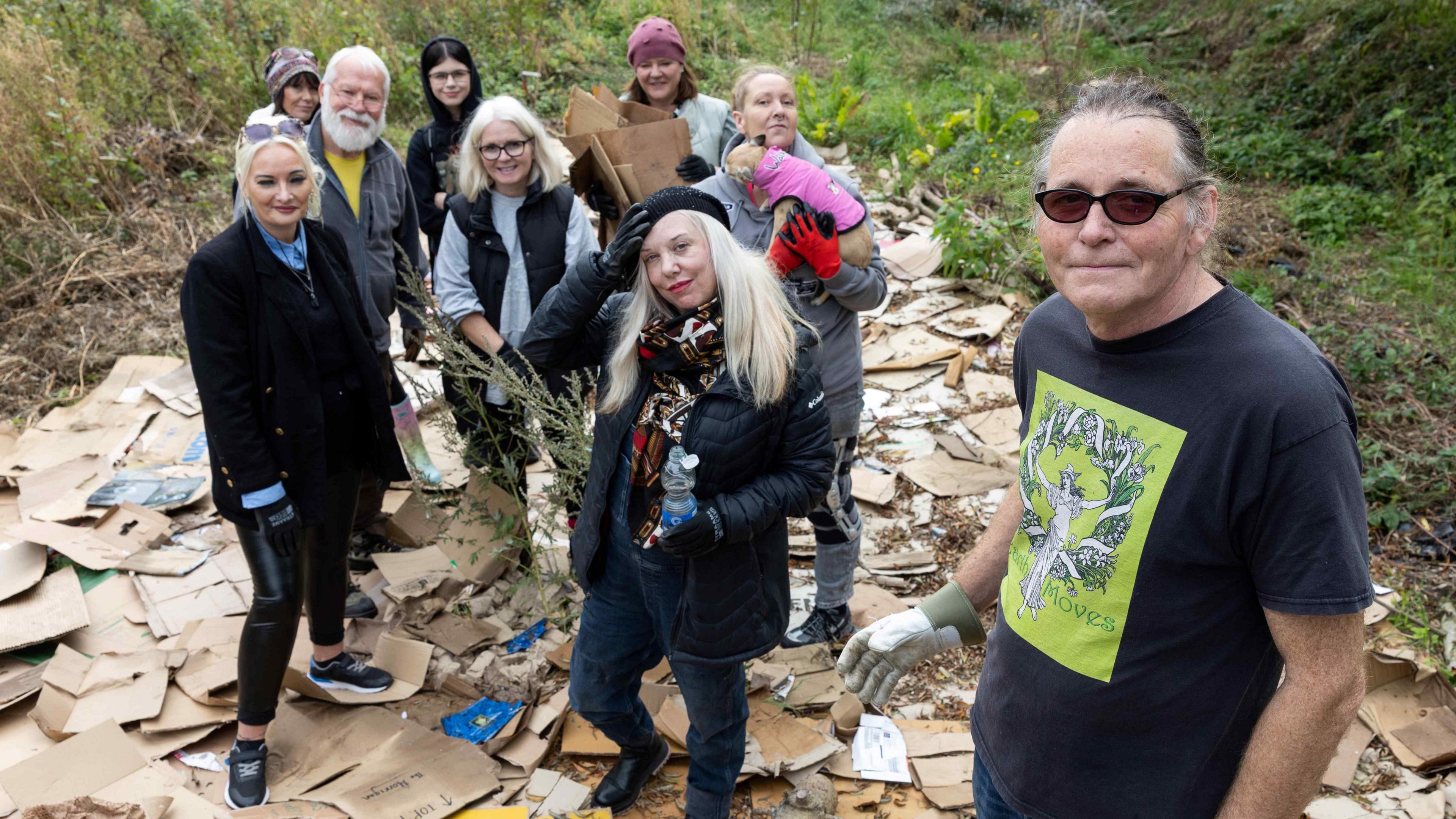 A wide shot of nine members of the Earth Moves group. They are standing on layers of cardboard which will eventually be used for compost.