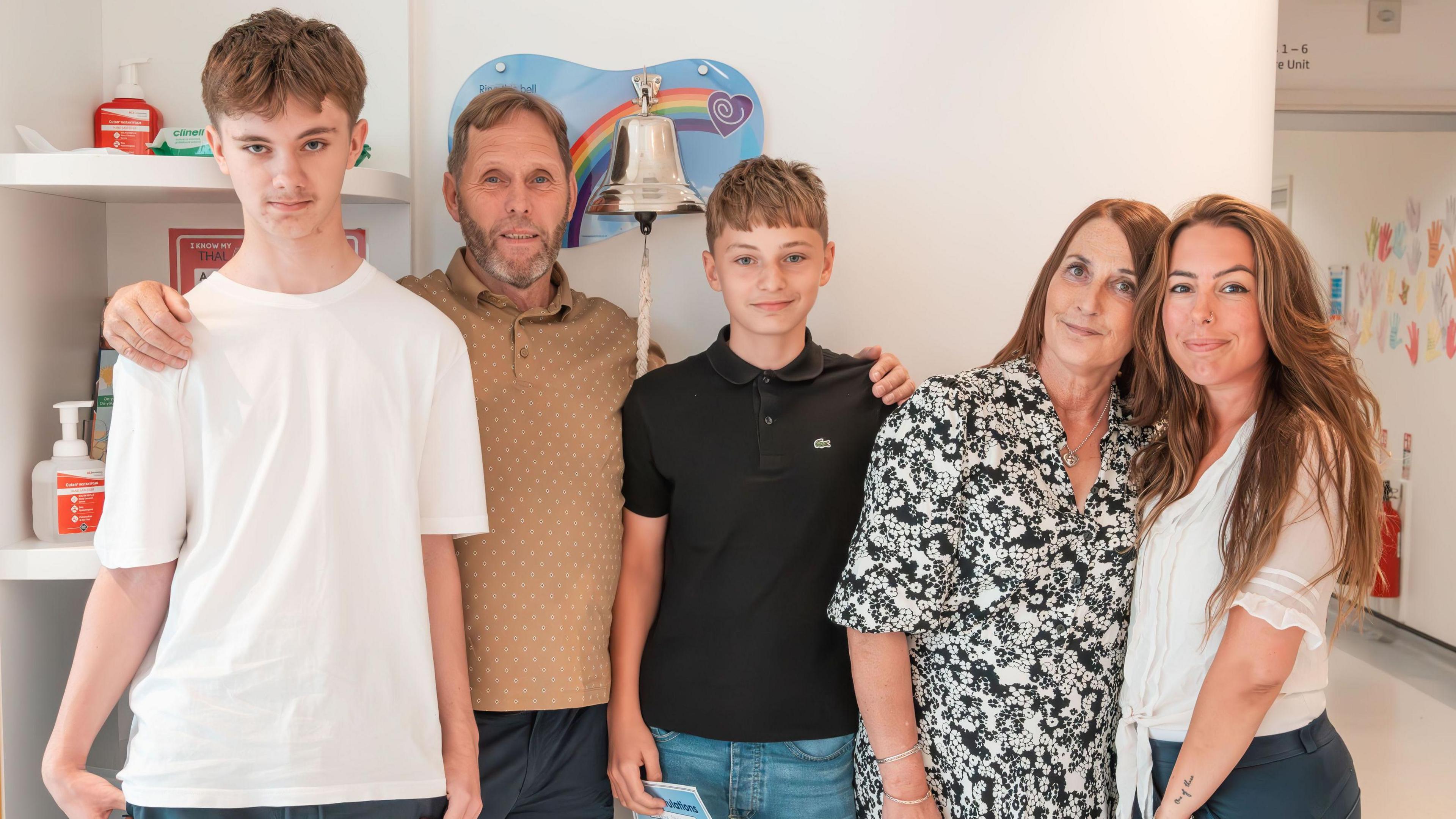 A photo of three men and two women stood next to a bell that is rung when somebody ends their cancer treatment