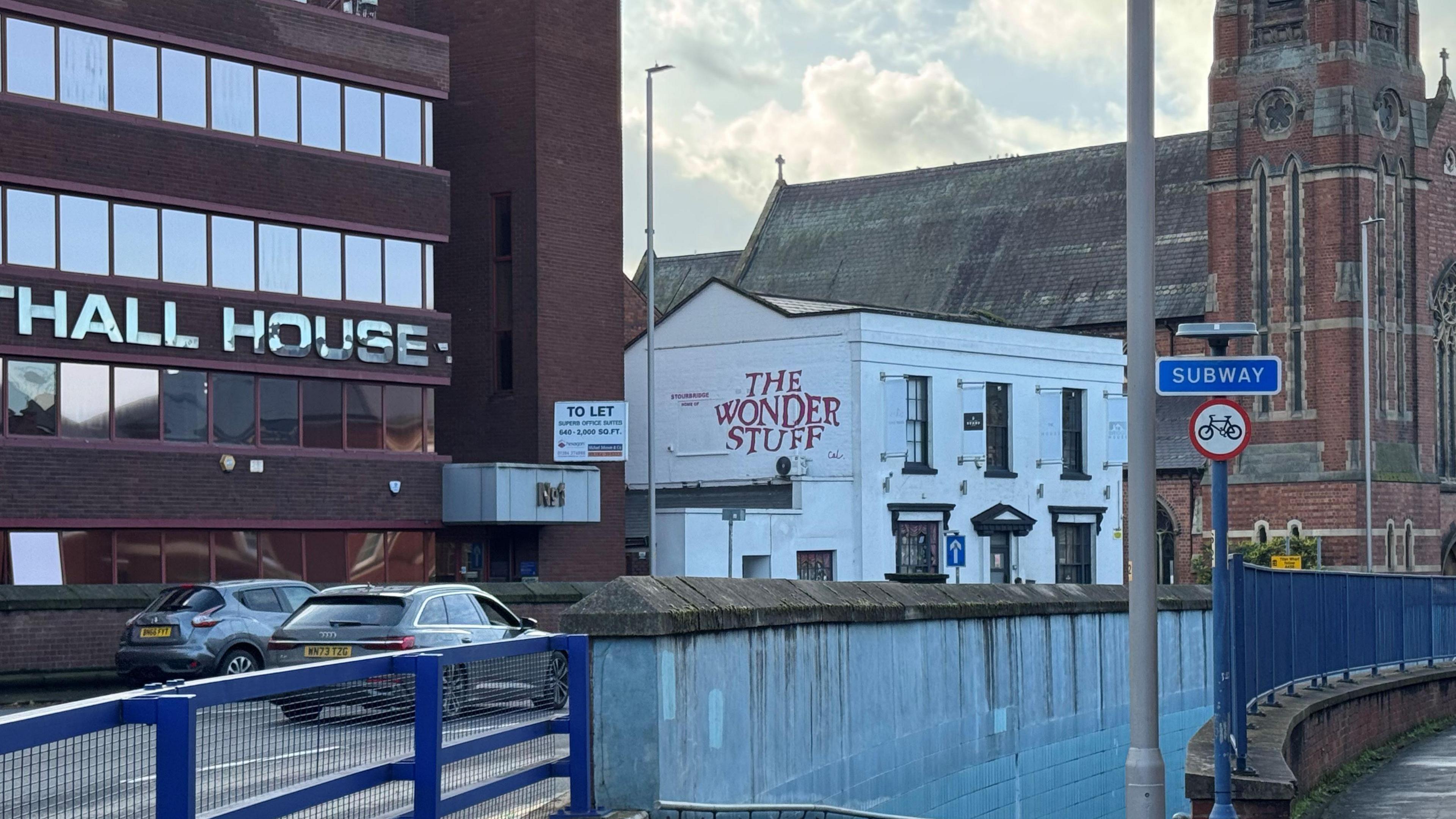 The Wonder Stuff mural on a white building which is next to a church and another building where part of the name can be seen 'Hall House'. 