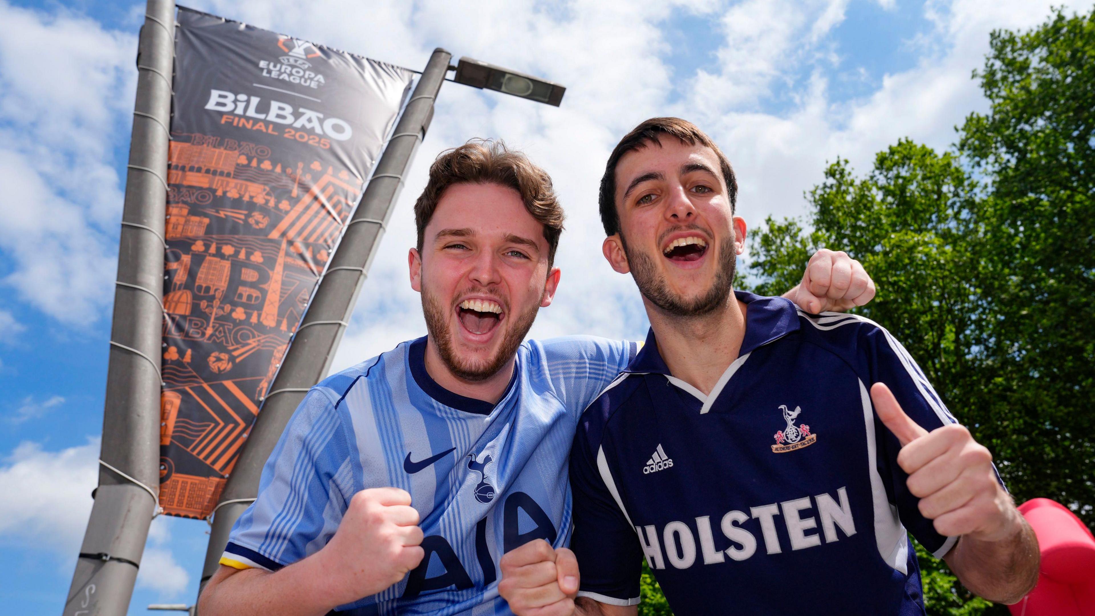 Two Tottenham fans cheer with a Europa League sign on a lamppost in the background