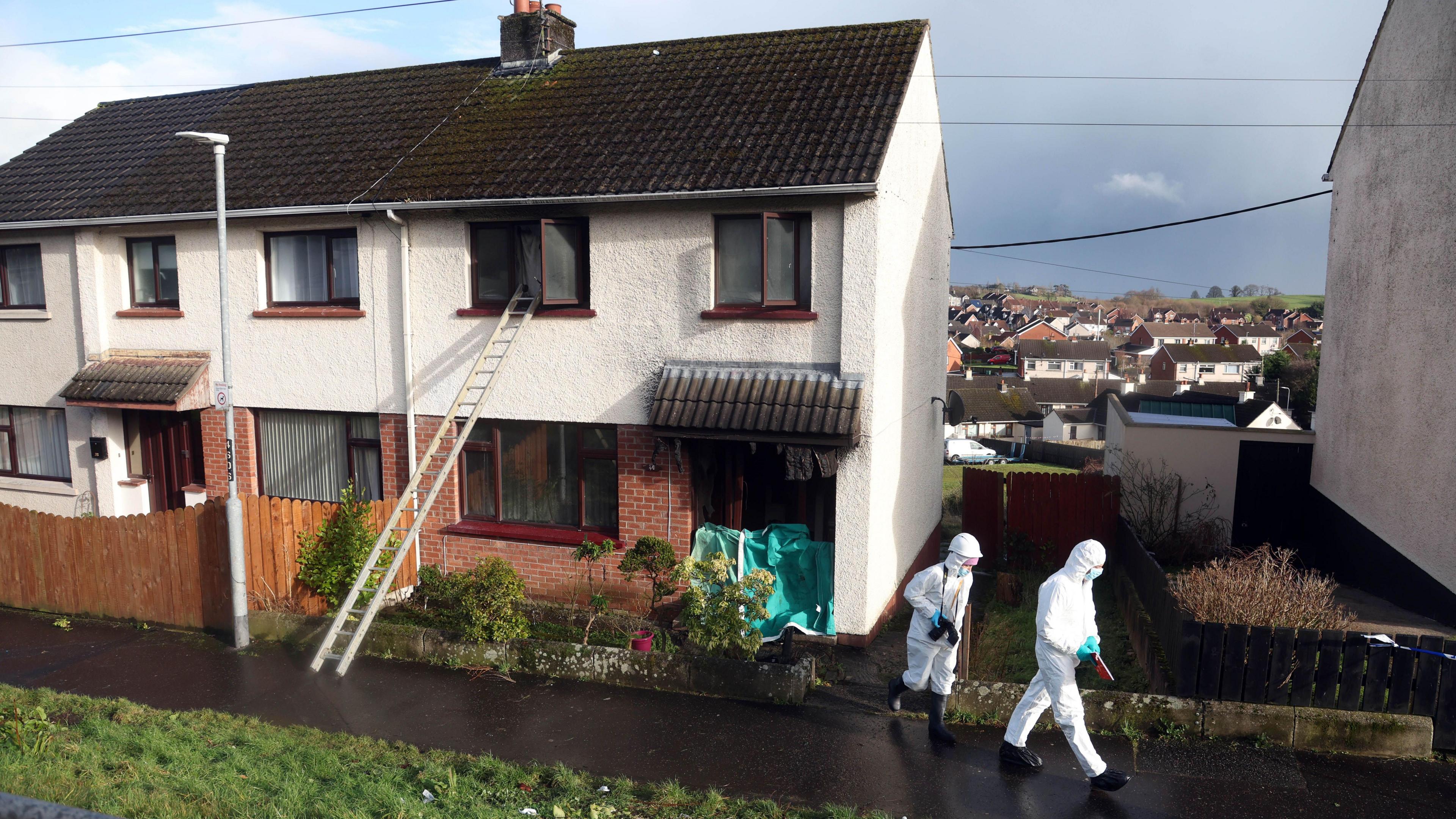 Two forensics officers in white suits walking outside burned house in Dunagnnon, with ladder stretching to open upstairs window