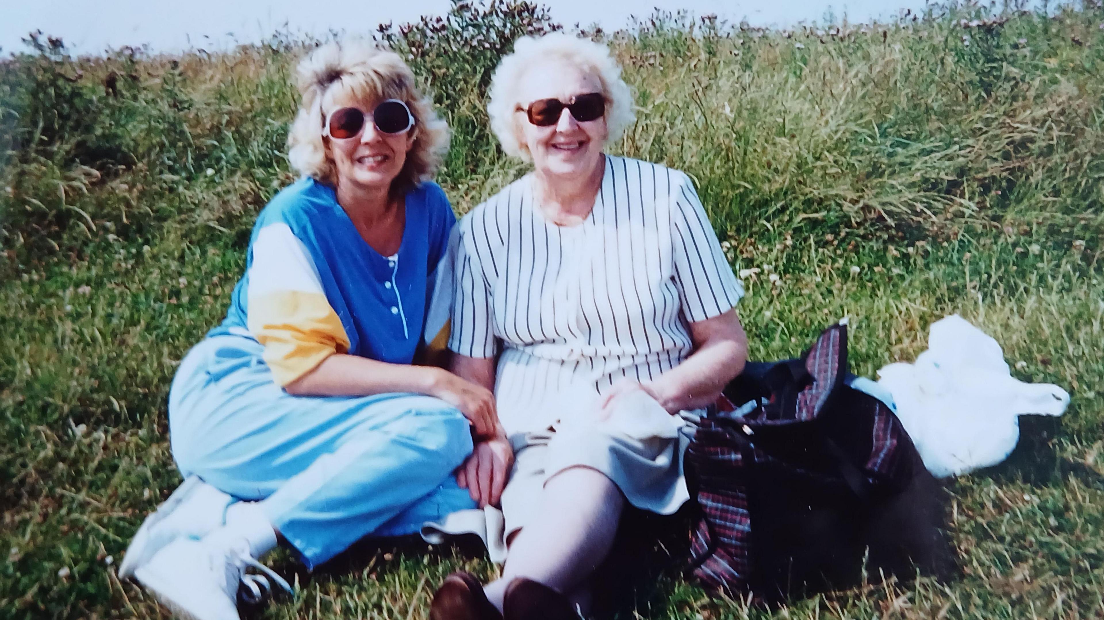 Judith and her mum siting on the grass in summer both smiling at the camera 