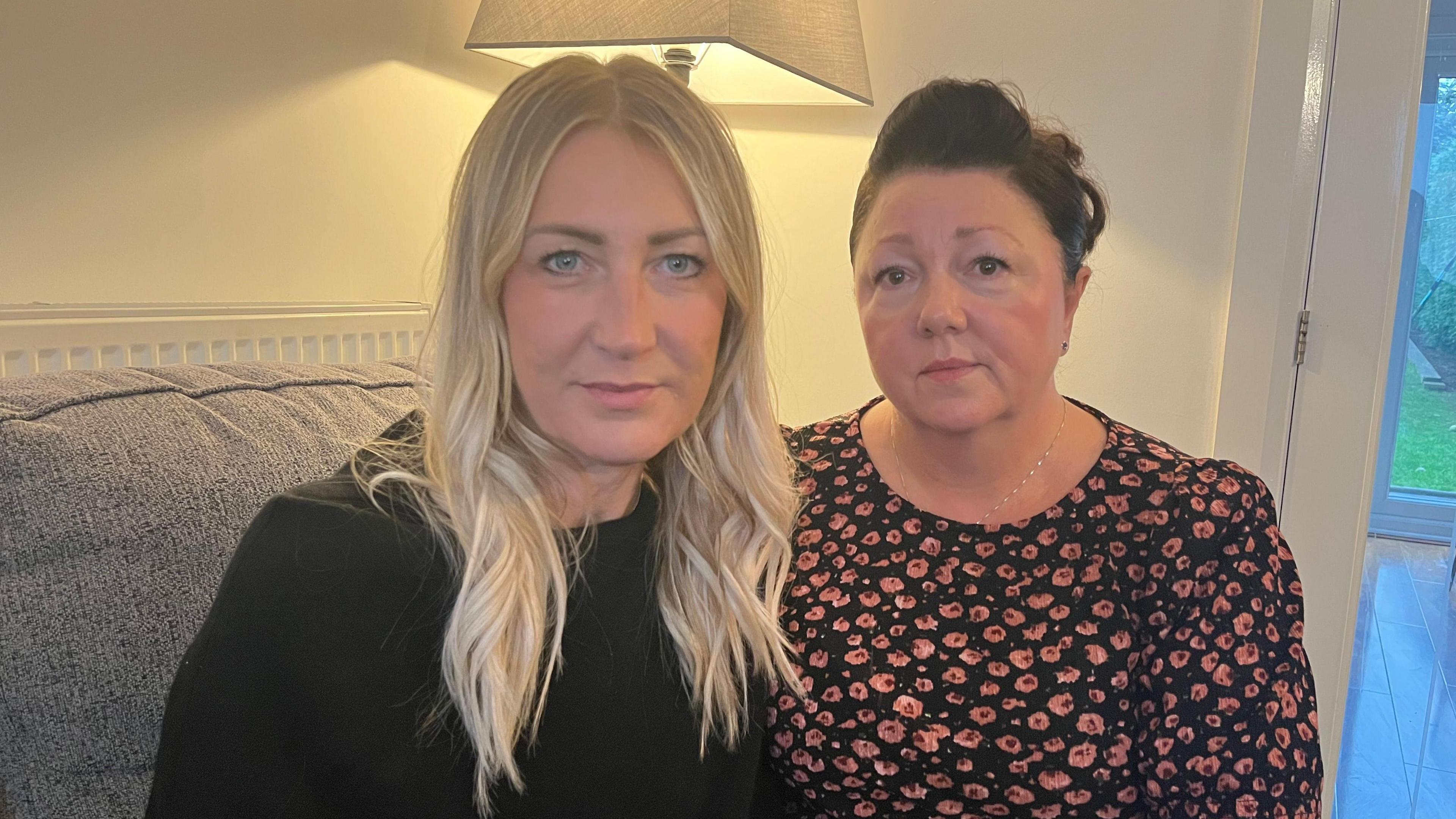 Melanie Meleshko and Lisa Wright sitting on a sofa looking at the camera