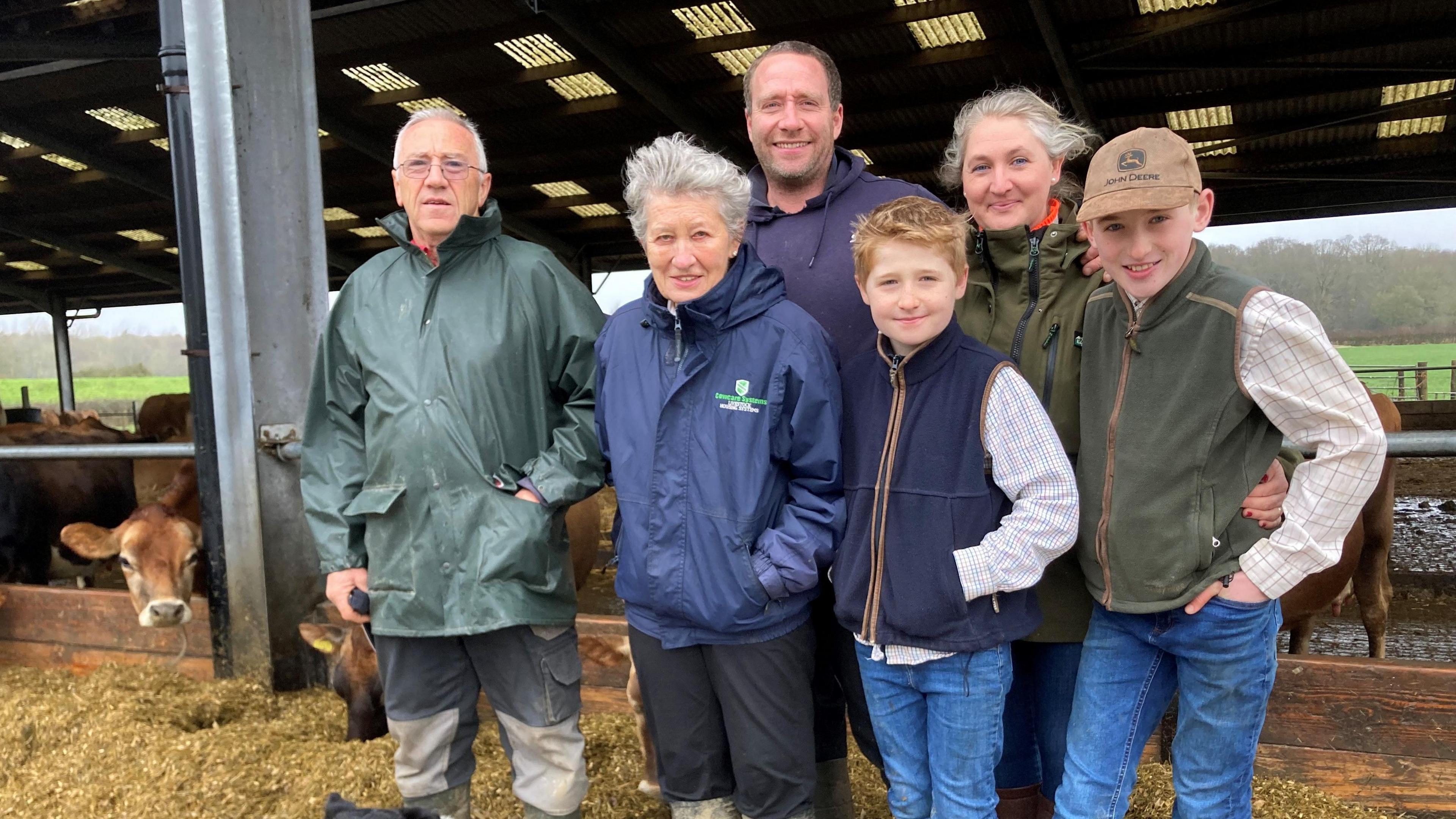 Six members of the same family - two men, two women and two boys - stand in front of a cow shed. 