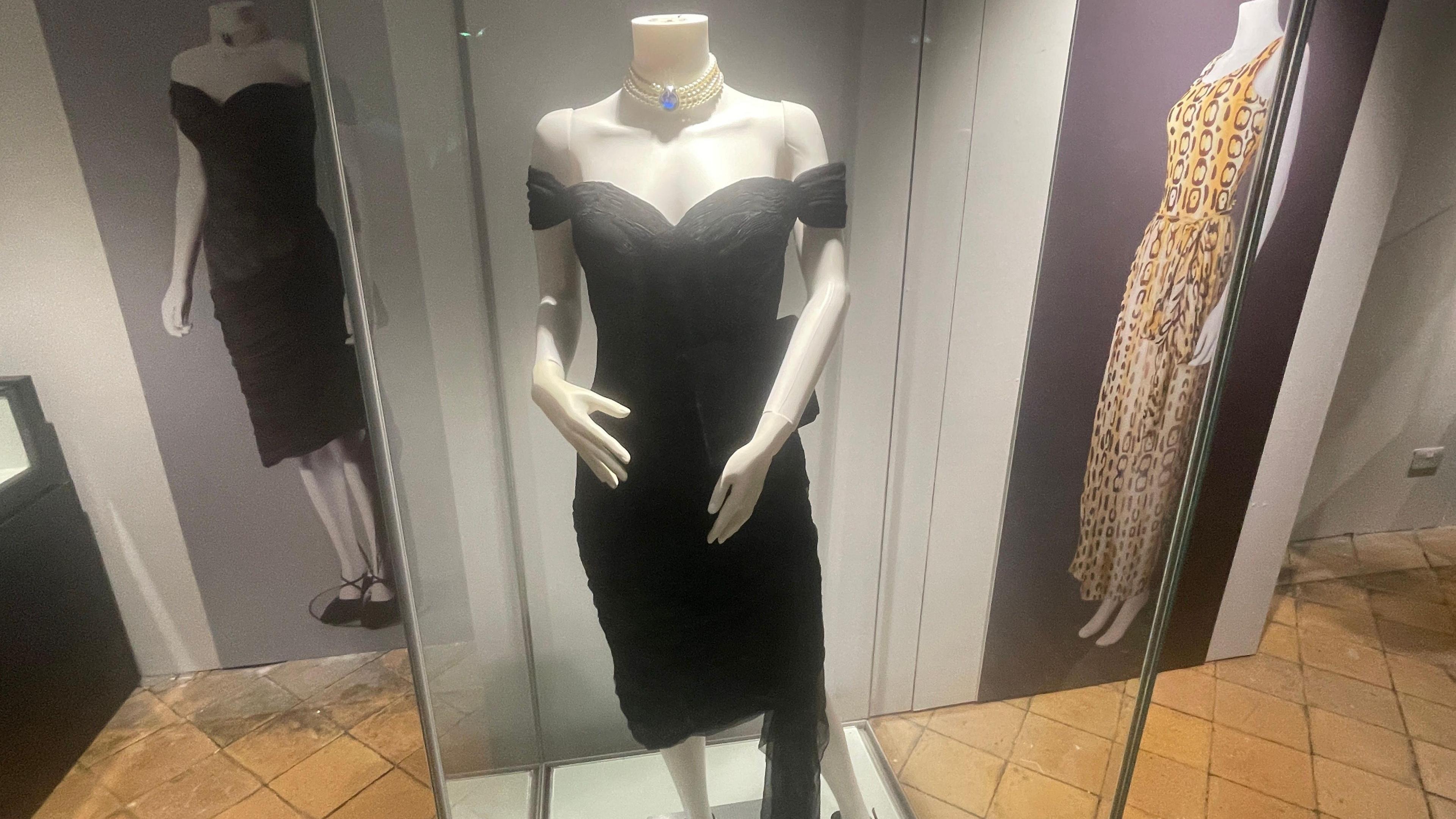 A mannequin in a glass display cabinet wearing a black dress