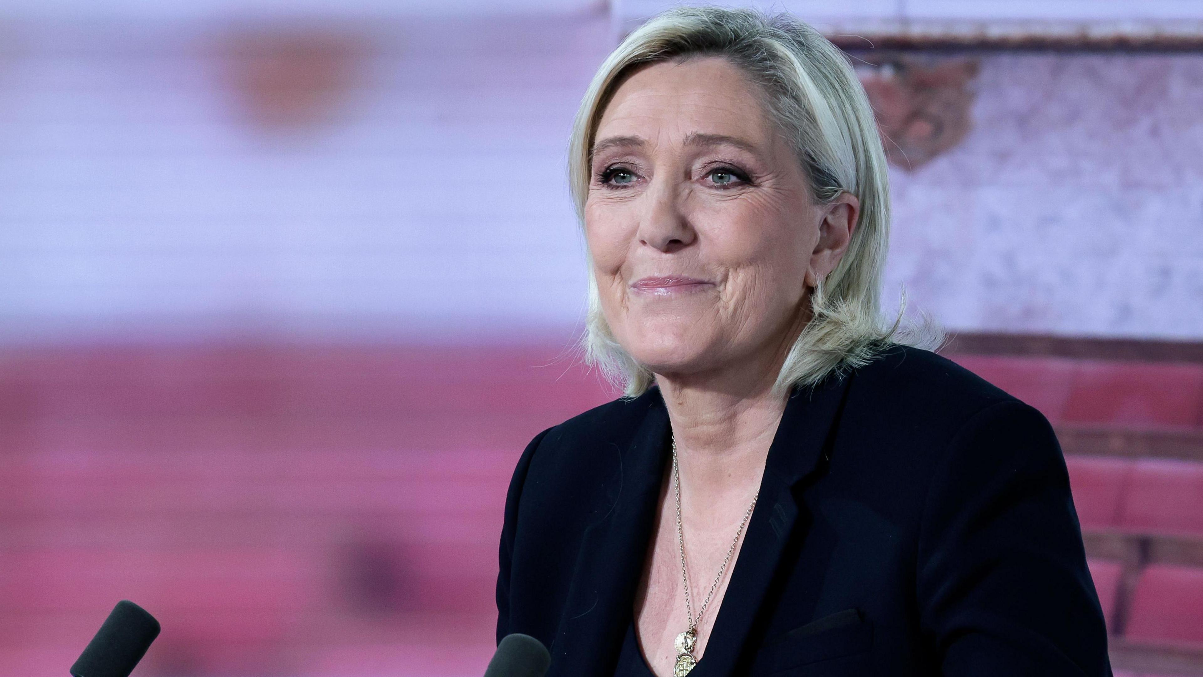 Marine Le Pen, who has a bleach blonde cropped bob and kohl-rimmed eyes, smiles as she is interviewed on a French TV channel