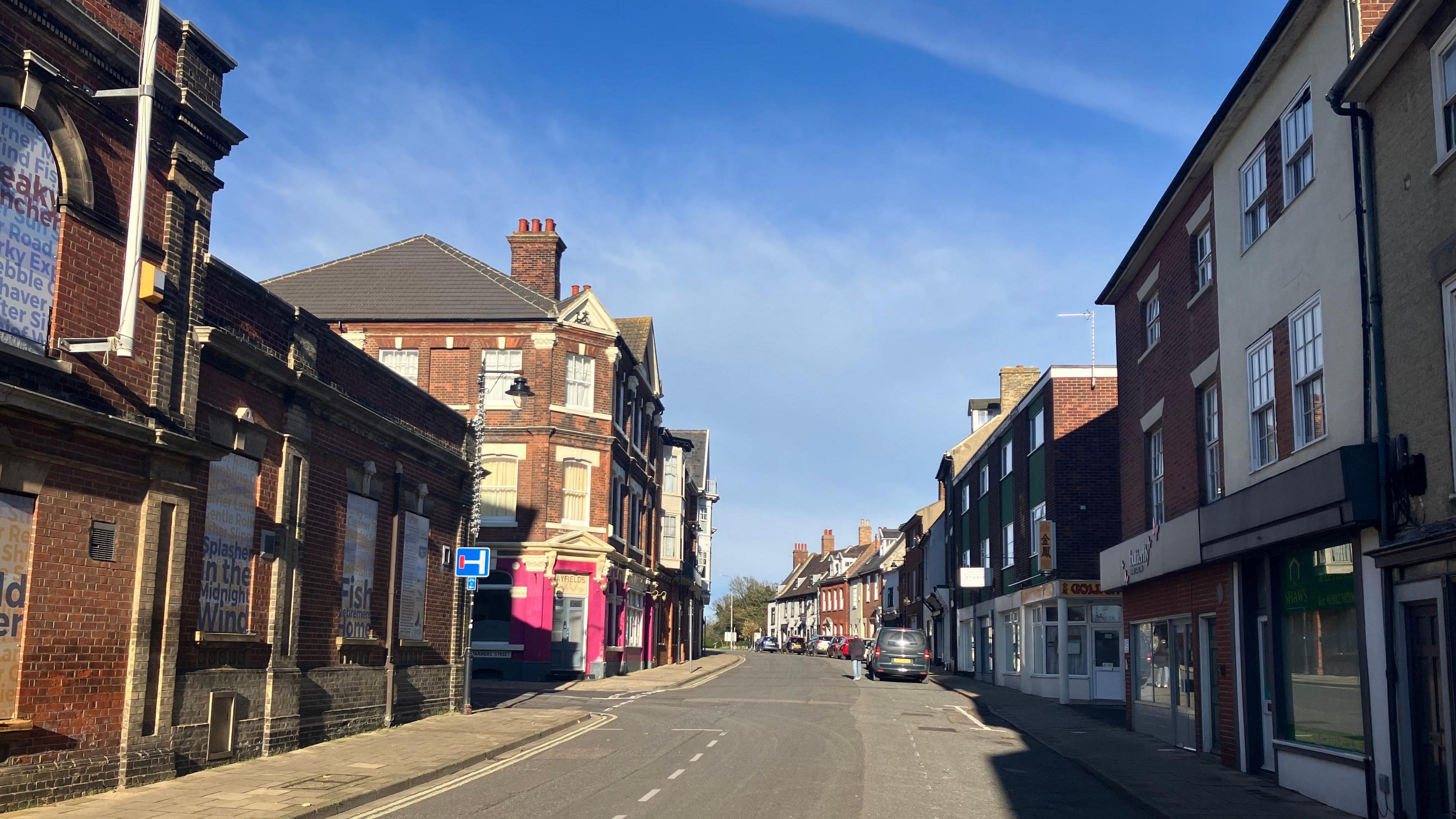 A view of Lowestoft's historic High Street showing the brick facade of the former Town Hall and various shop fronts and parked cars in the distance 