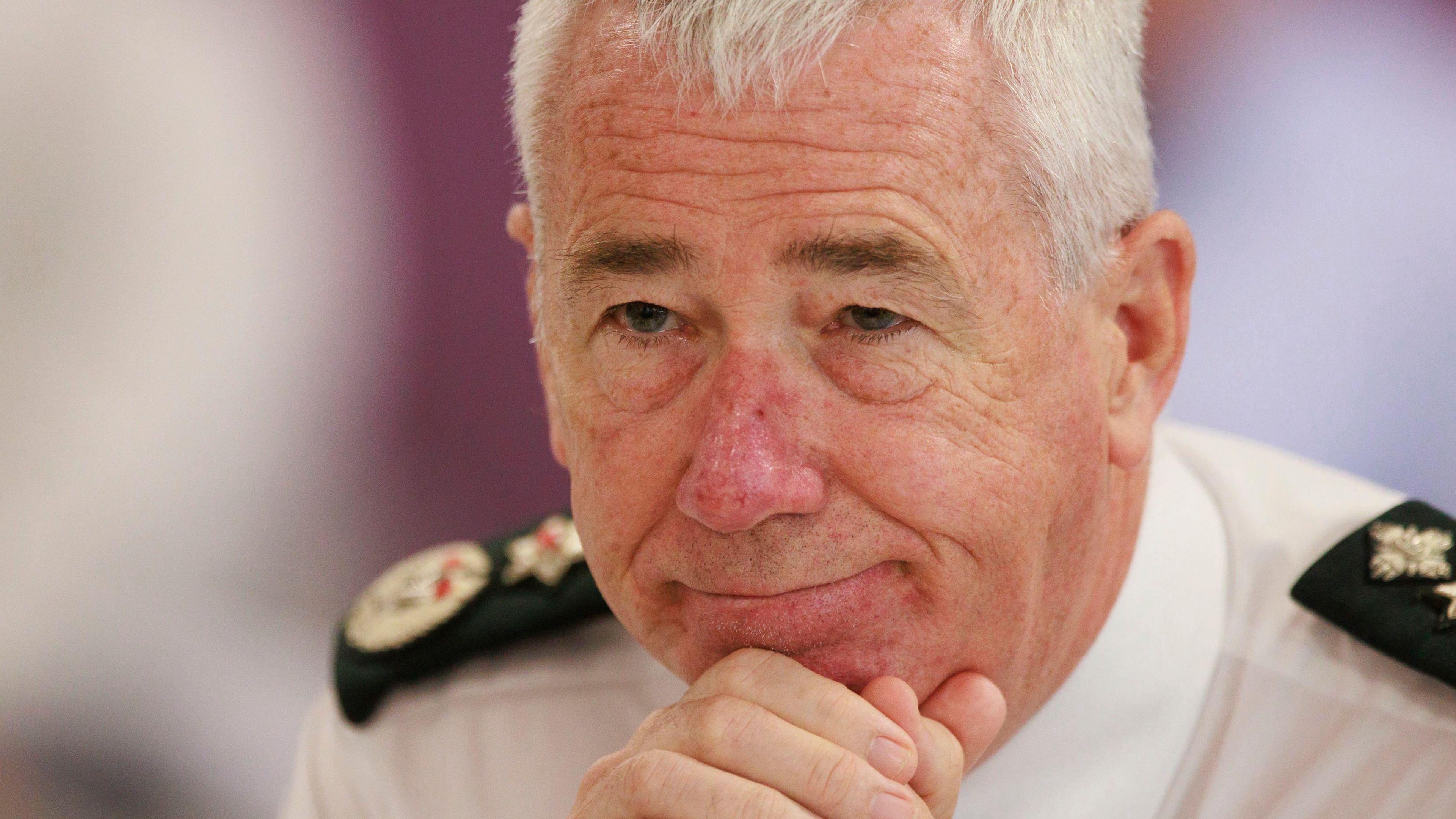 Jon Boutcher who has short white hair and is holding his head in clenched hands. He is wearing a PSNI uniform - white shirt. He is being asked a question and is not looking at the camera. 