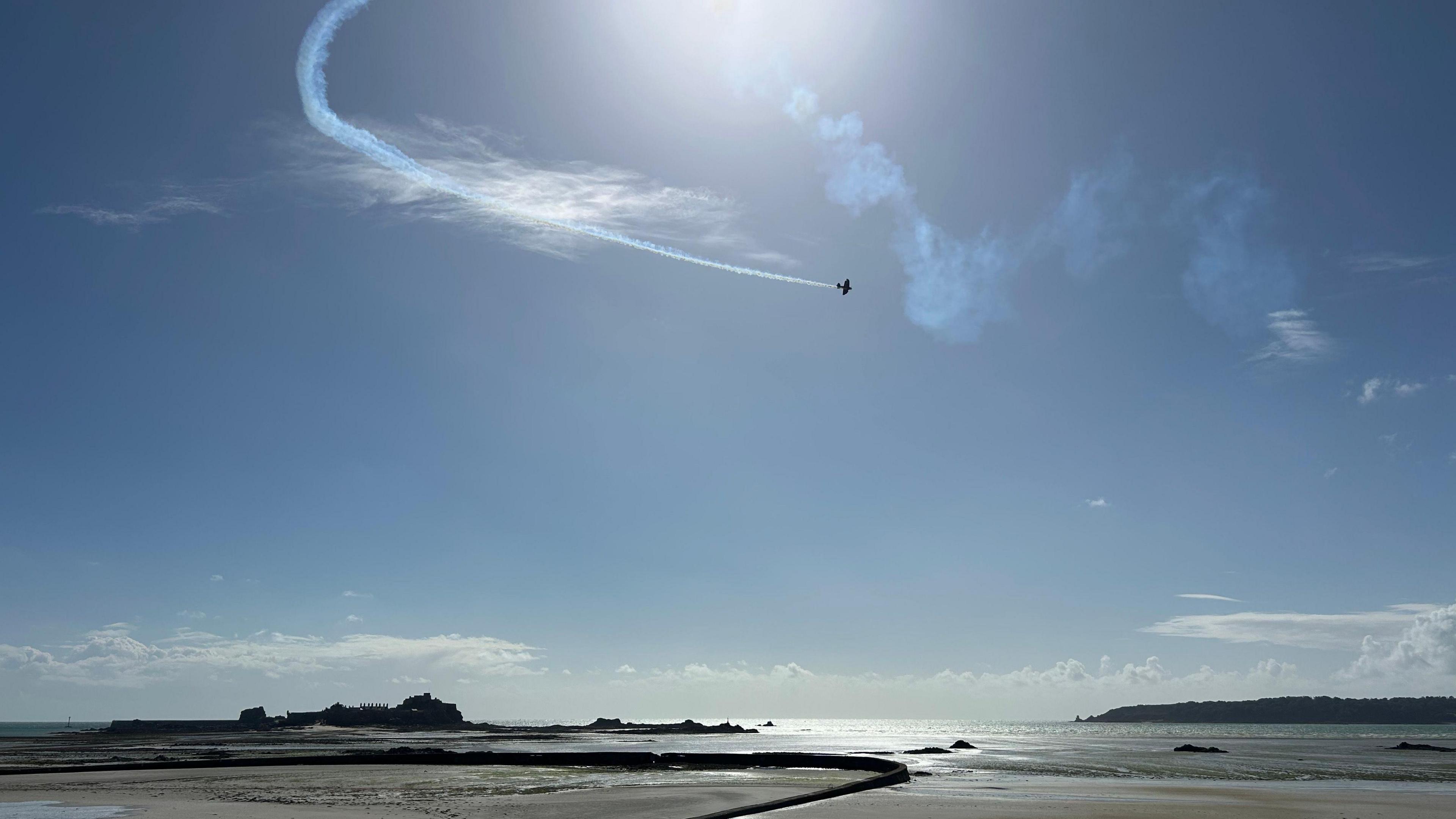 A plane in the mostly-cloudless sky above a wide sandy beach.