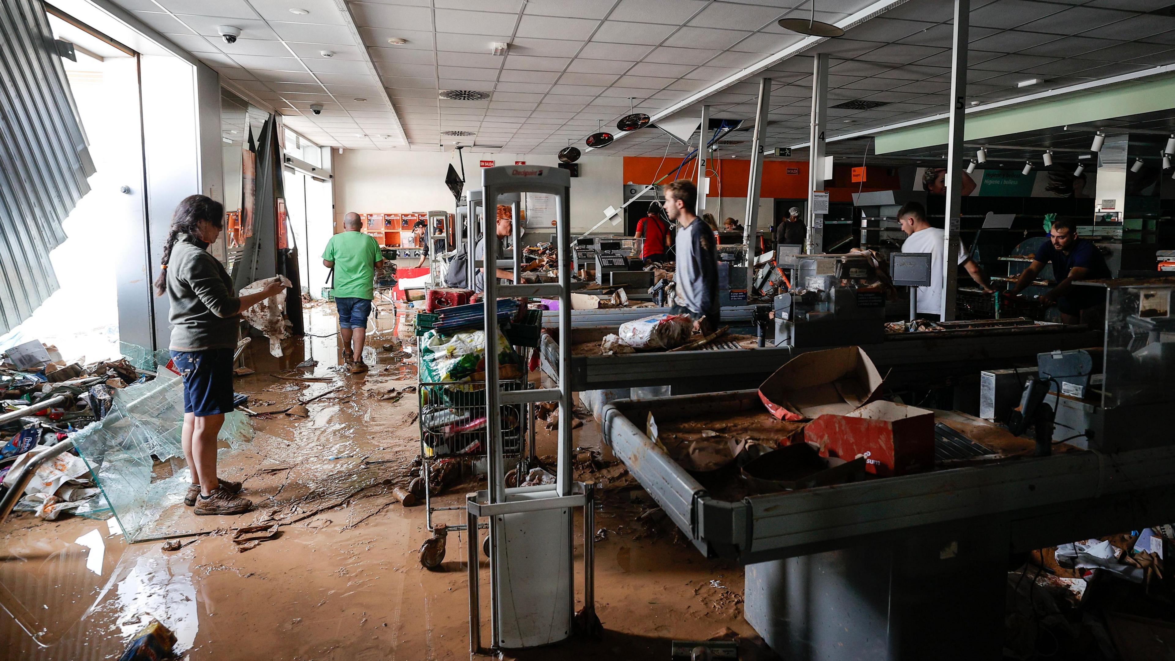 The image shows the inside of a supermarket where many people try to clear up the mess and damage the flooding has caused. 