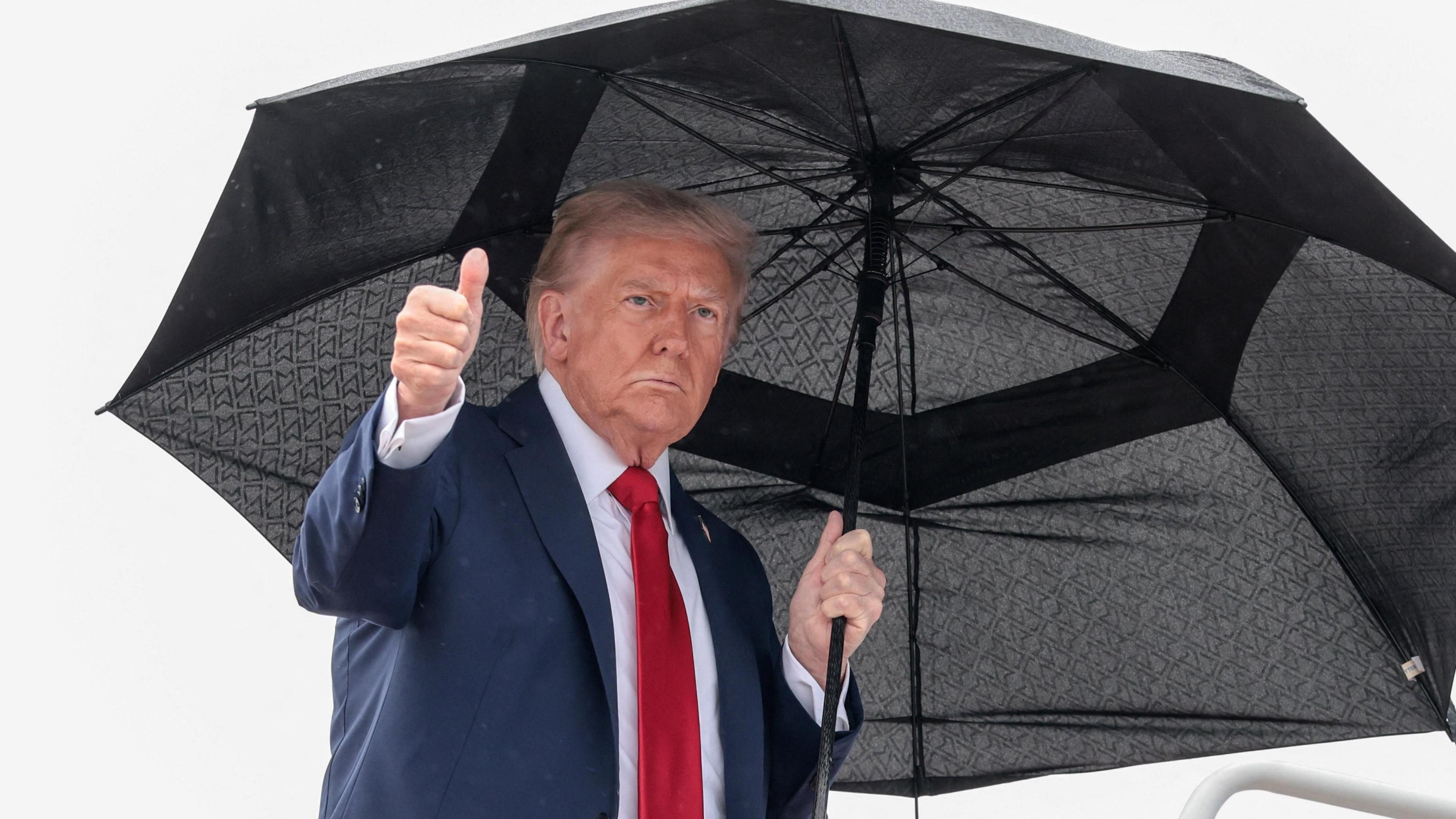 US President Donald Trump gives a thumbs up from under a black umbrella, while boarding Air Force One for his trip to Israel.