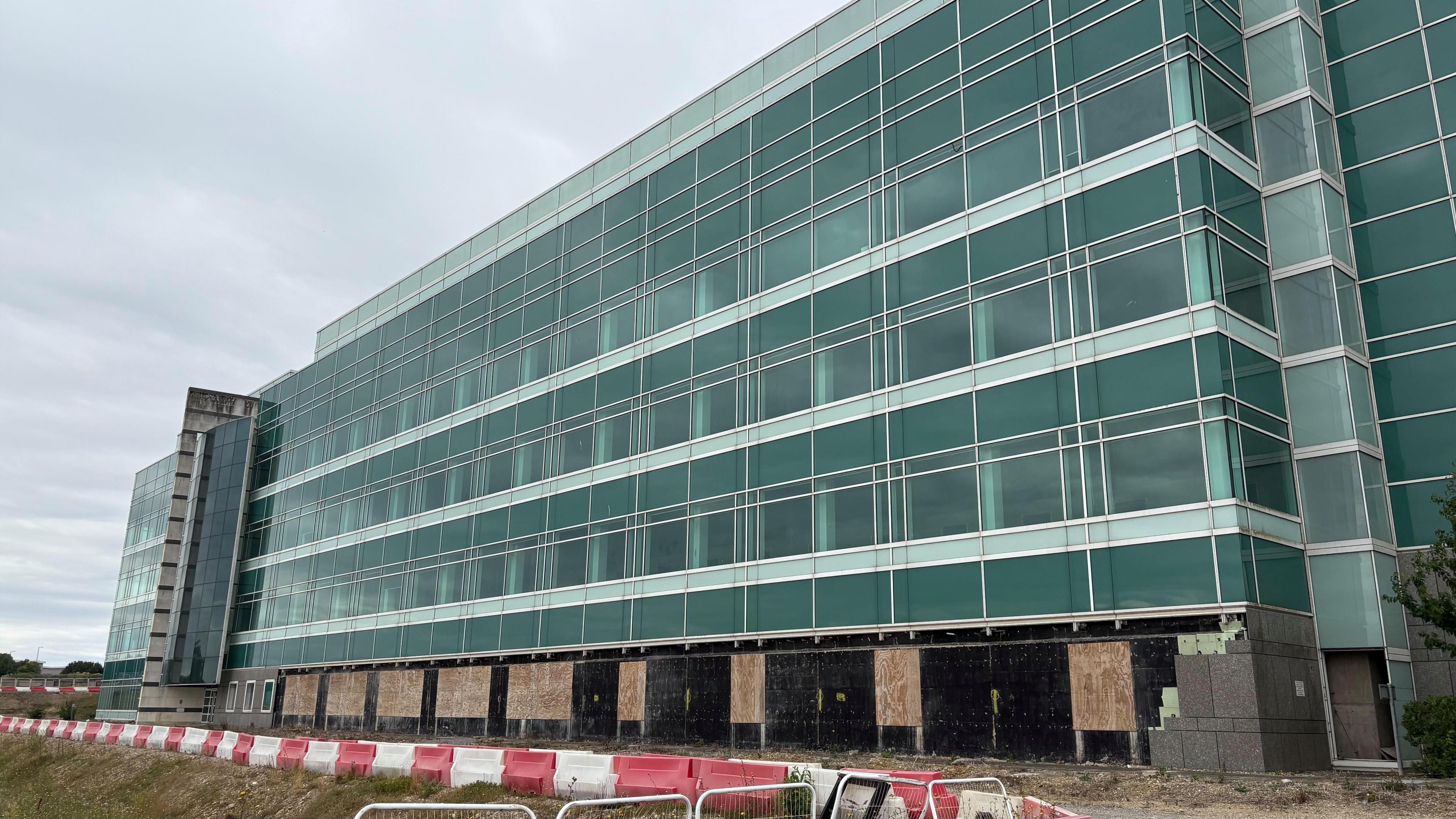 Modern multi-story building with glass windows, the ground floor us under construction with boarded-up sections.