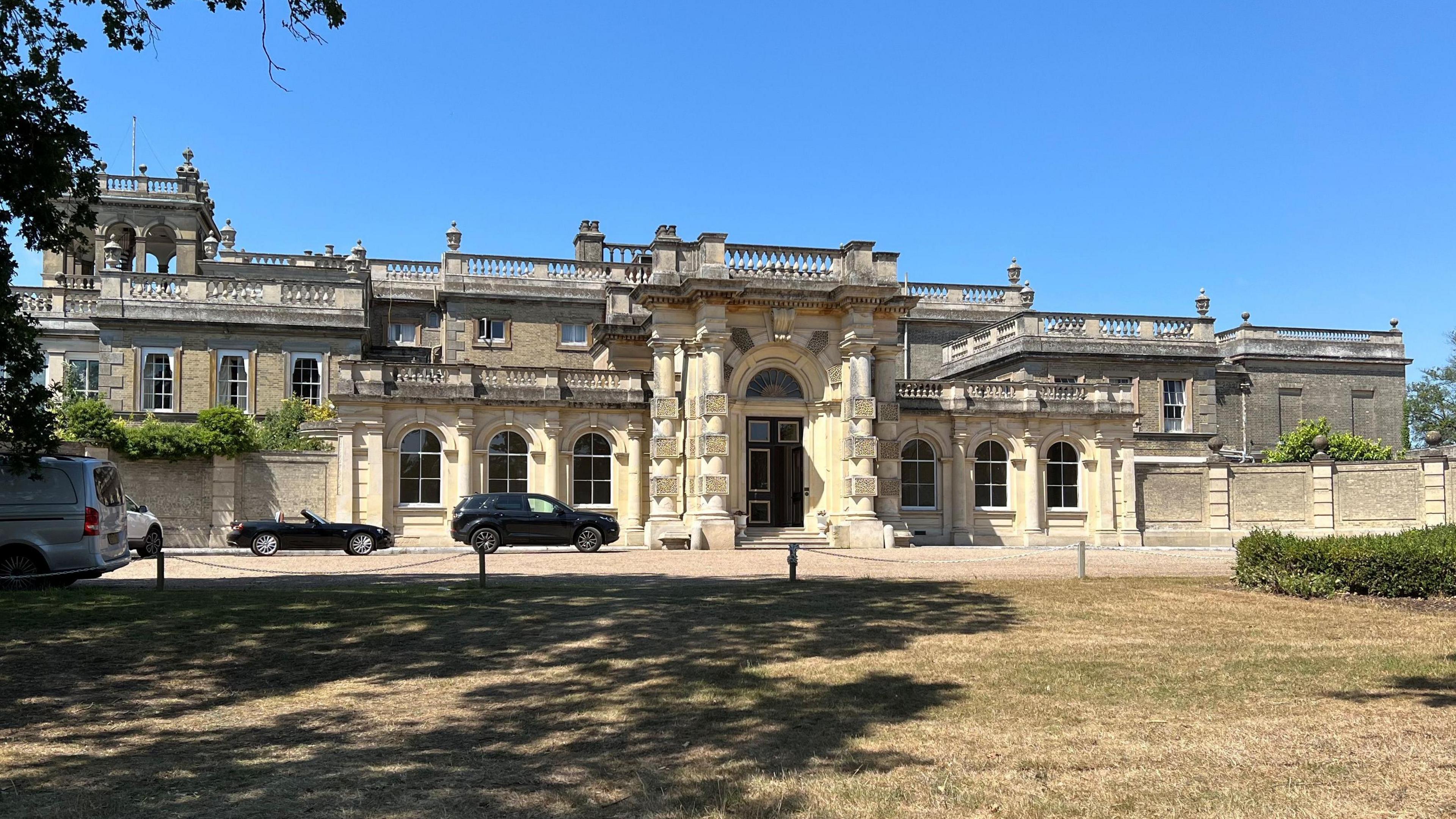 The outside of Shrubland Hall, which is a historic English country house. The sky is blue with no clouds.