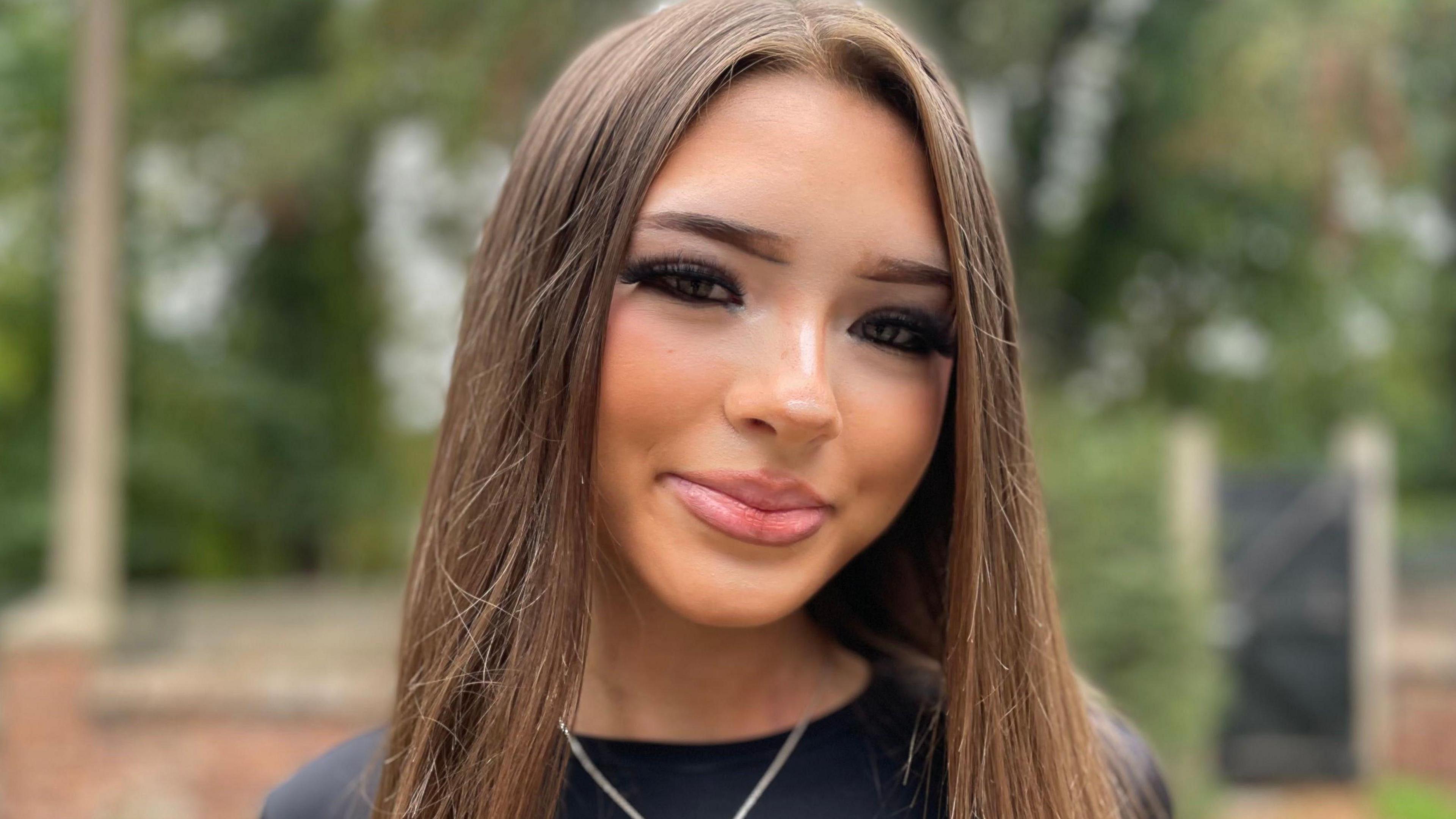 Teenage girl with long brown hair wearing a black top and silver cross