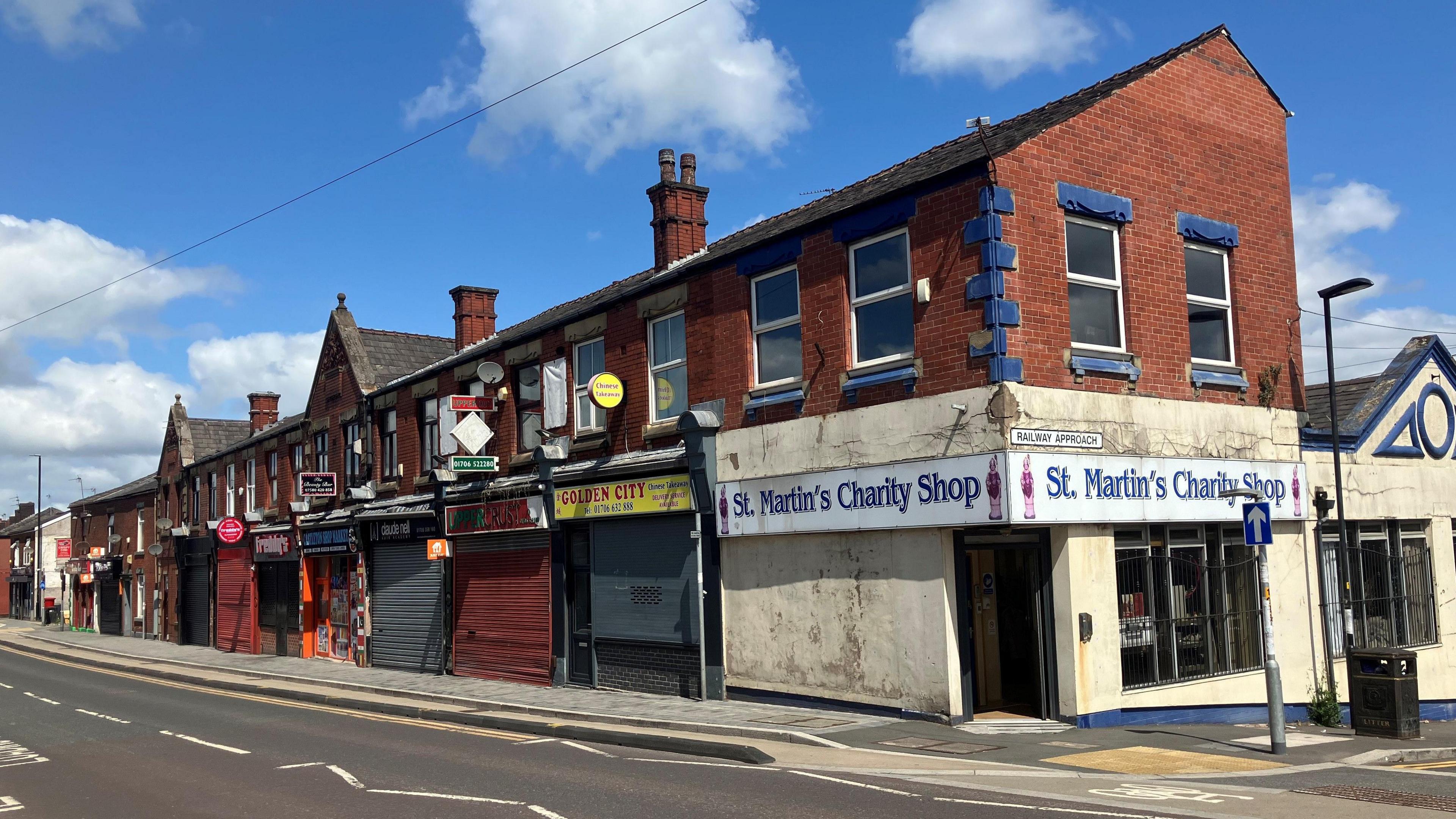 Photograph of shops on Manchester Road in Castleton. Many of the businesses have closed - or have their metal shutters drawn down.