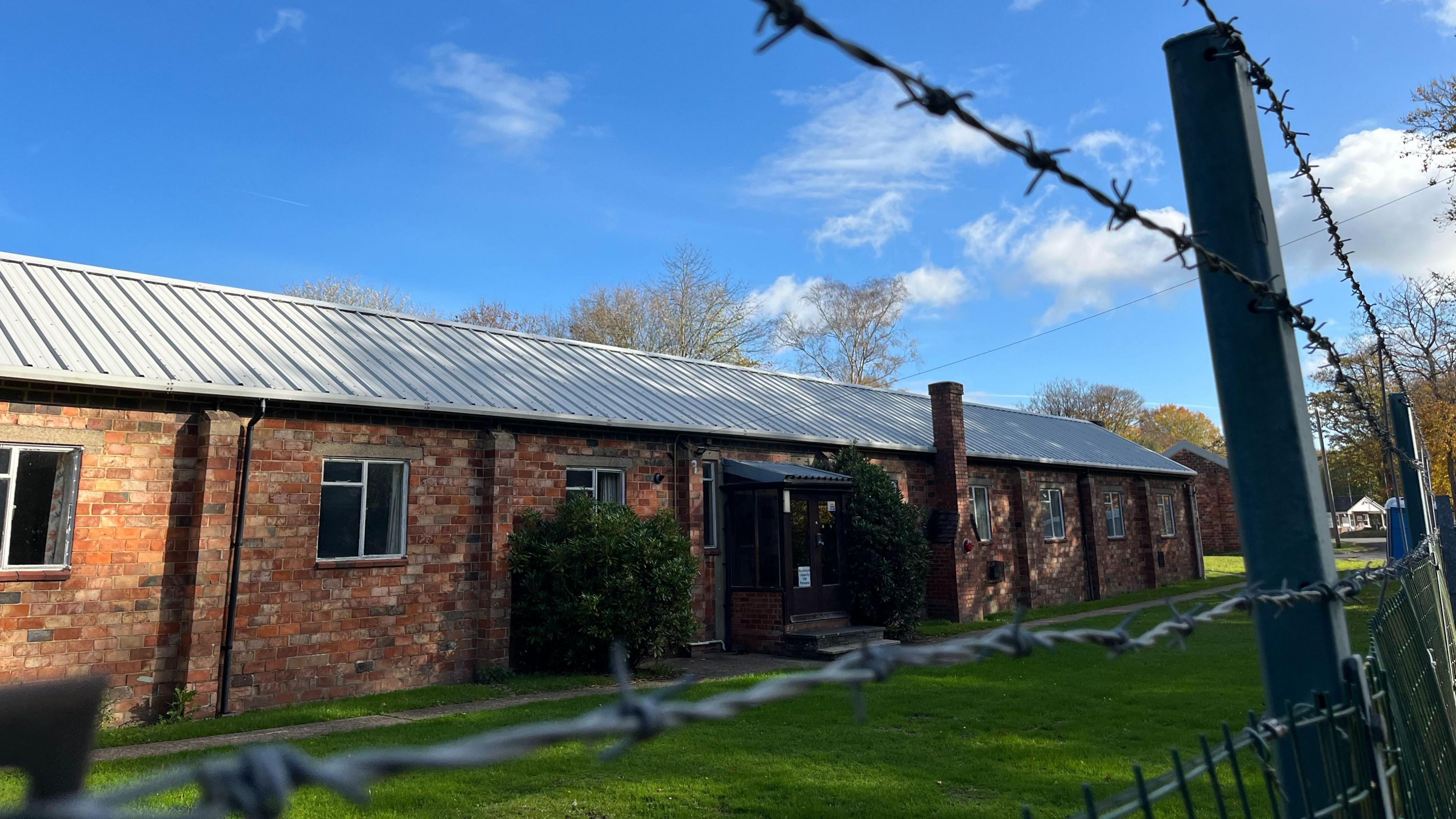 A red-bricked military building. Barbed wire is in front of it.