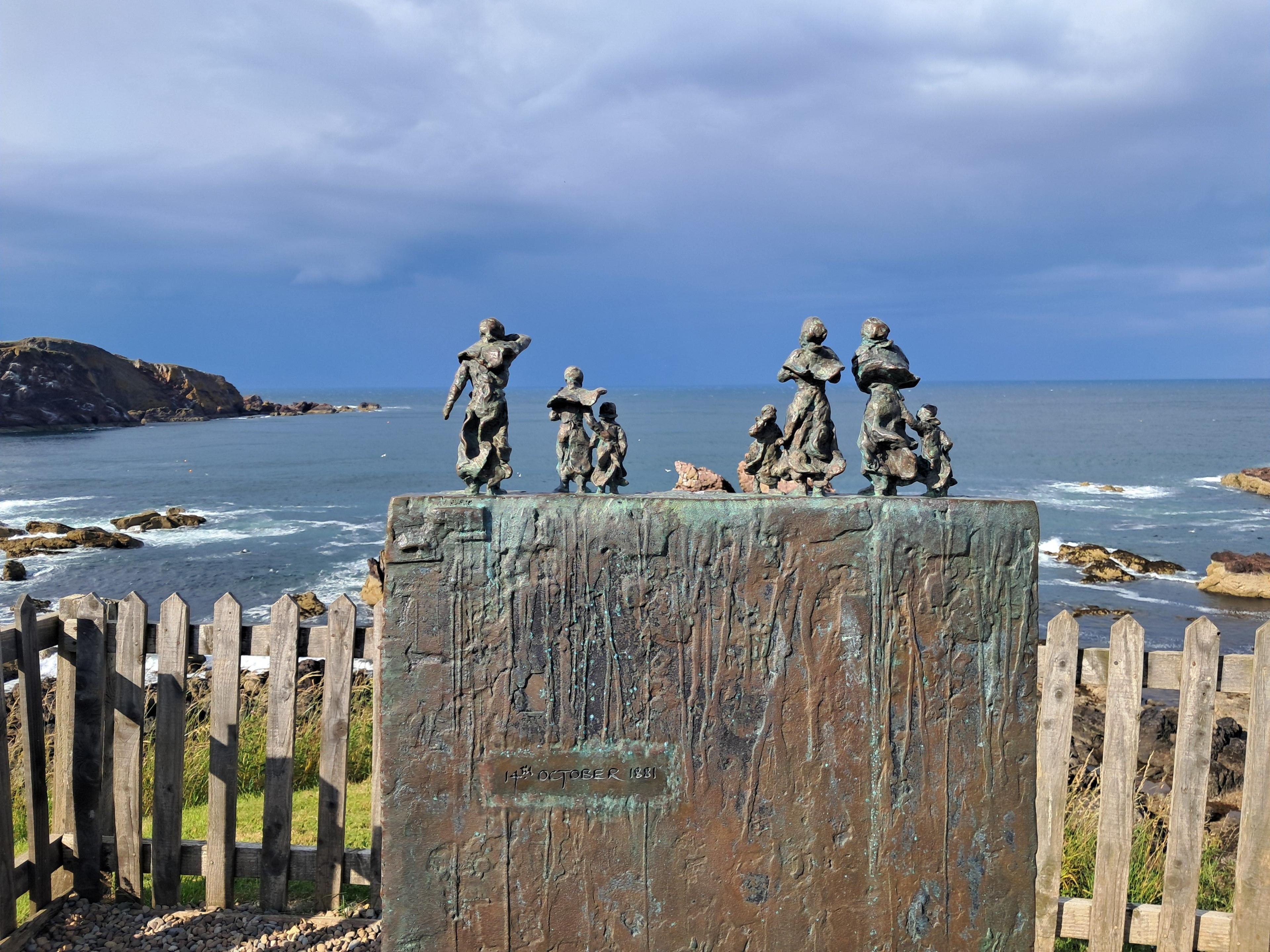 A sculpture sitting overlooking the sea, with several small figures placed on it