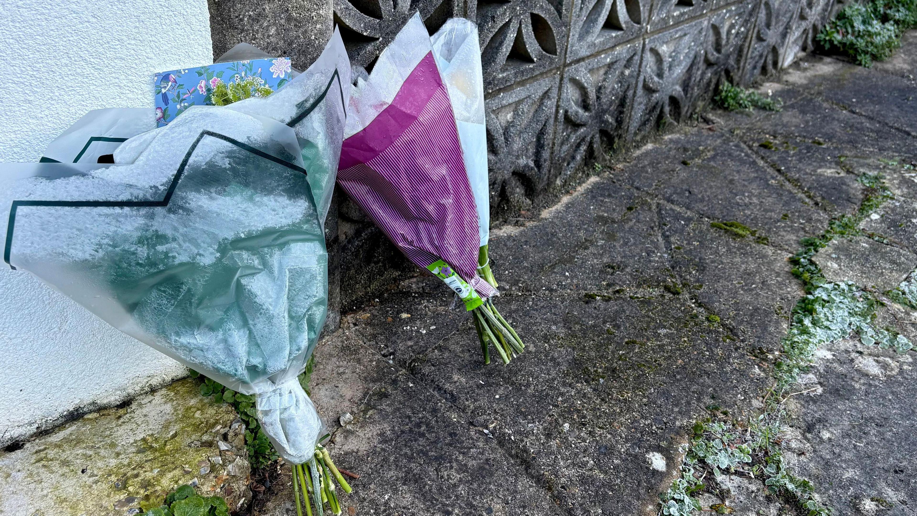 Two bunches of flowers resting against a wall on the street floor