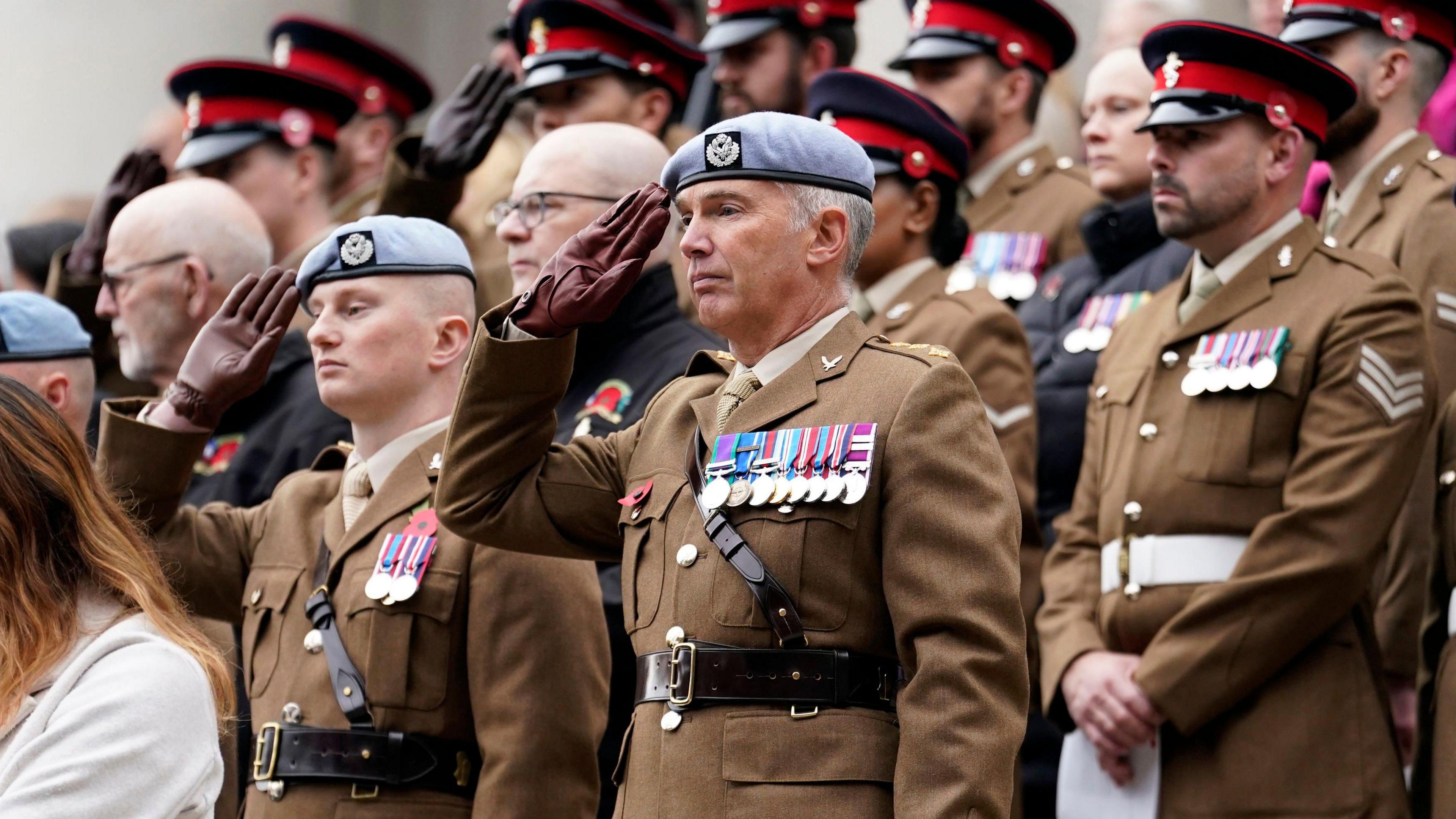 Members of the armed forces are dressed in military uniform with medals on their chests and hats on their heads. They are saluting.