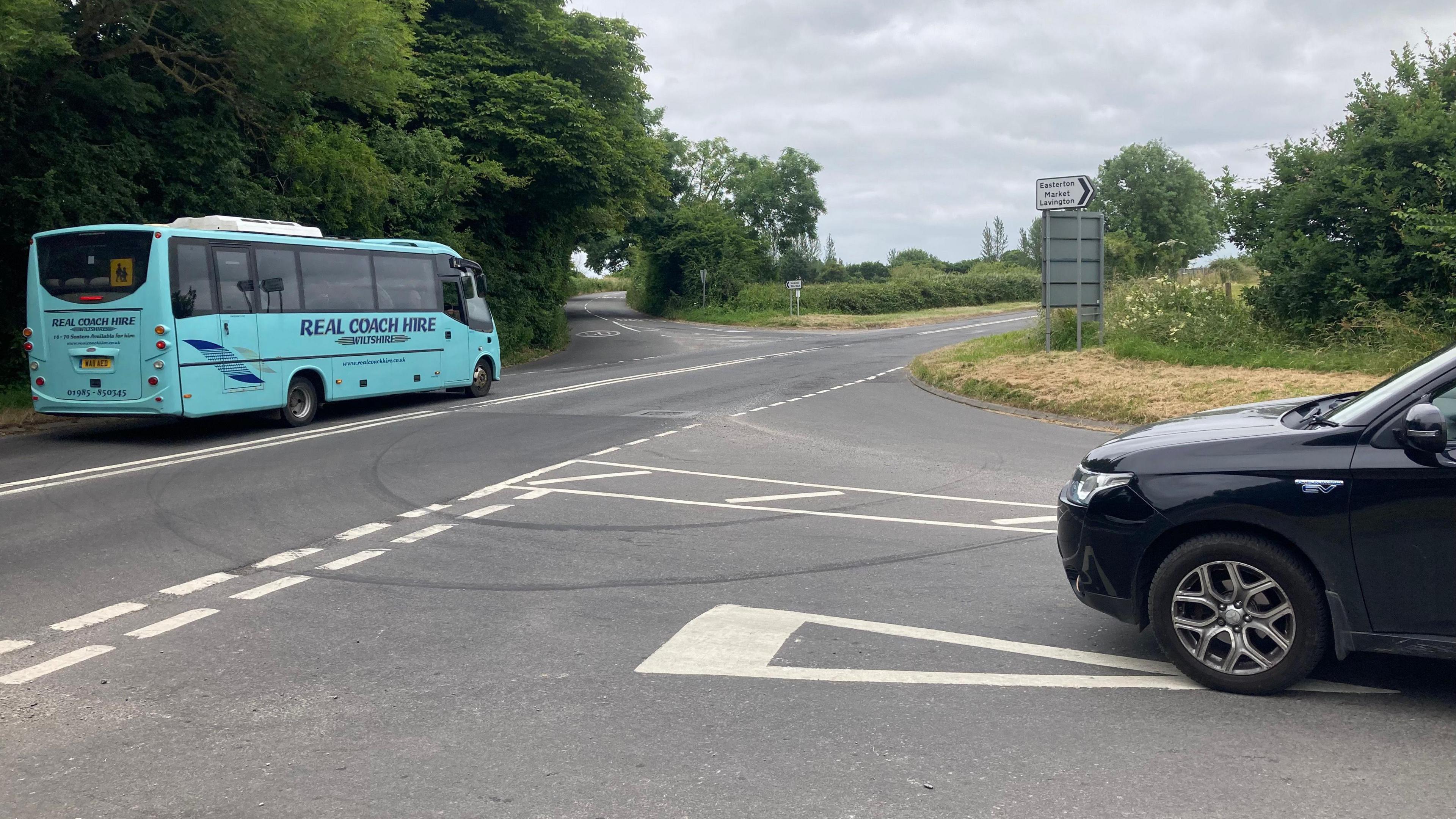 A black car approaching the give away lines at a cross roads and a blue coach travelling along the main road