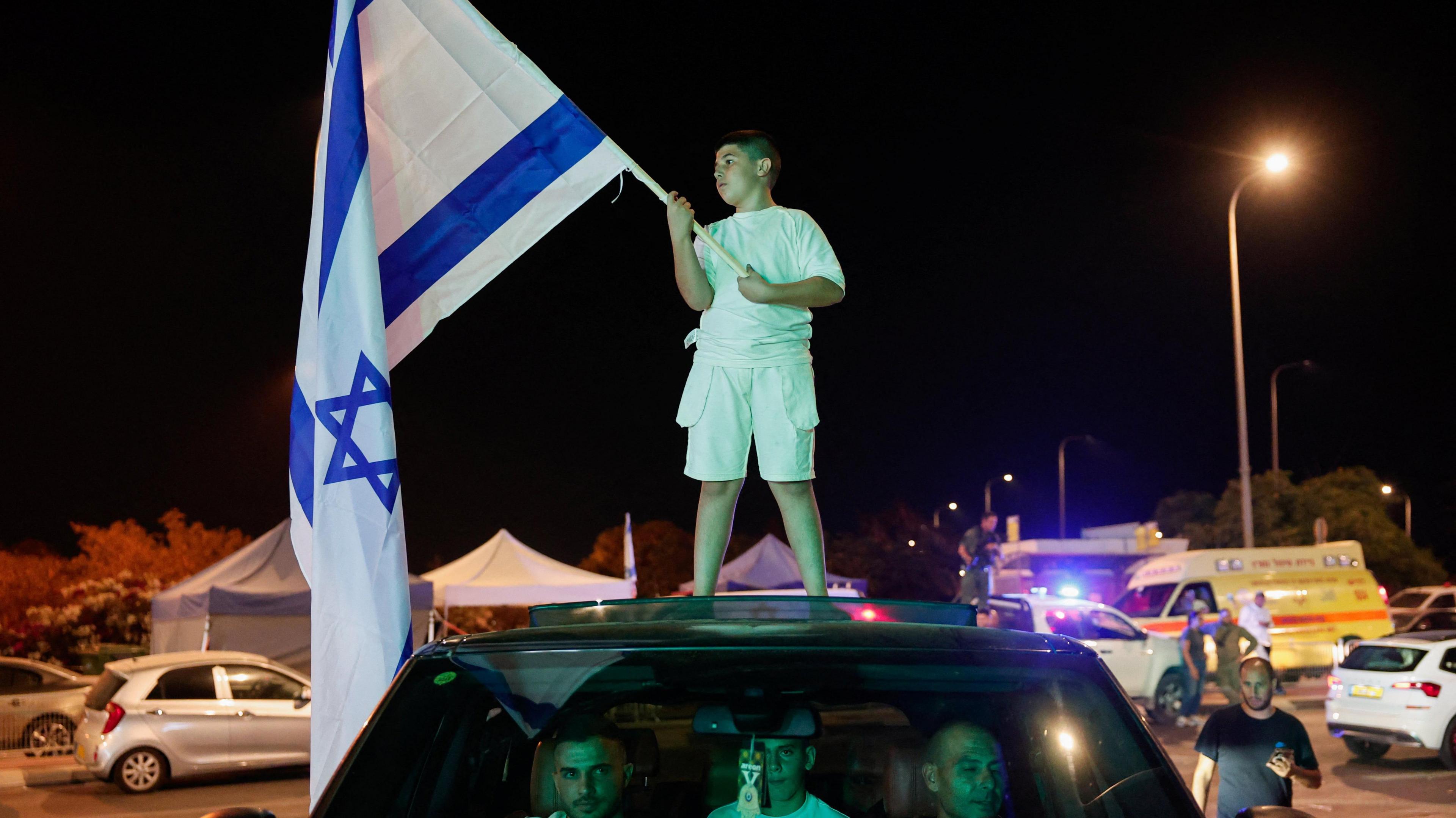 A boy holds an Israeli flag while standing on top of a car at night. after Israeli military said they have killed Hamas leader Yahya Sinwar, in Sderot, Israel, October 17, 2024.