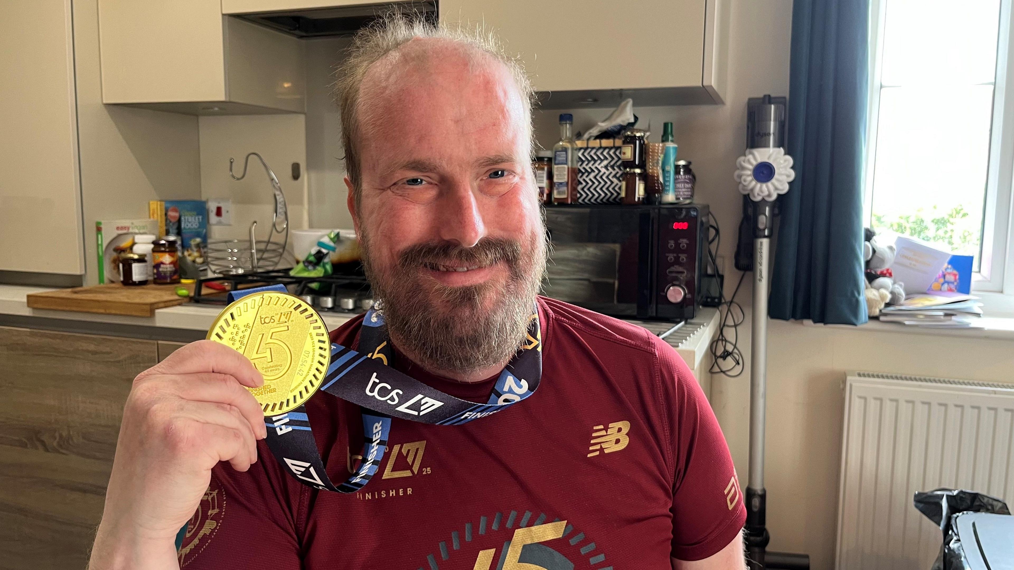 Nathaniel Dye, 39, smiles as he holds a marathon winner's medal around his neck sitting at the kitchen table in his flat