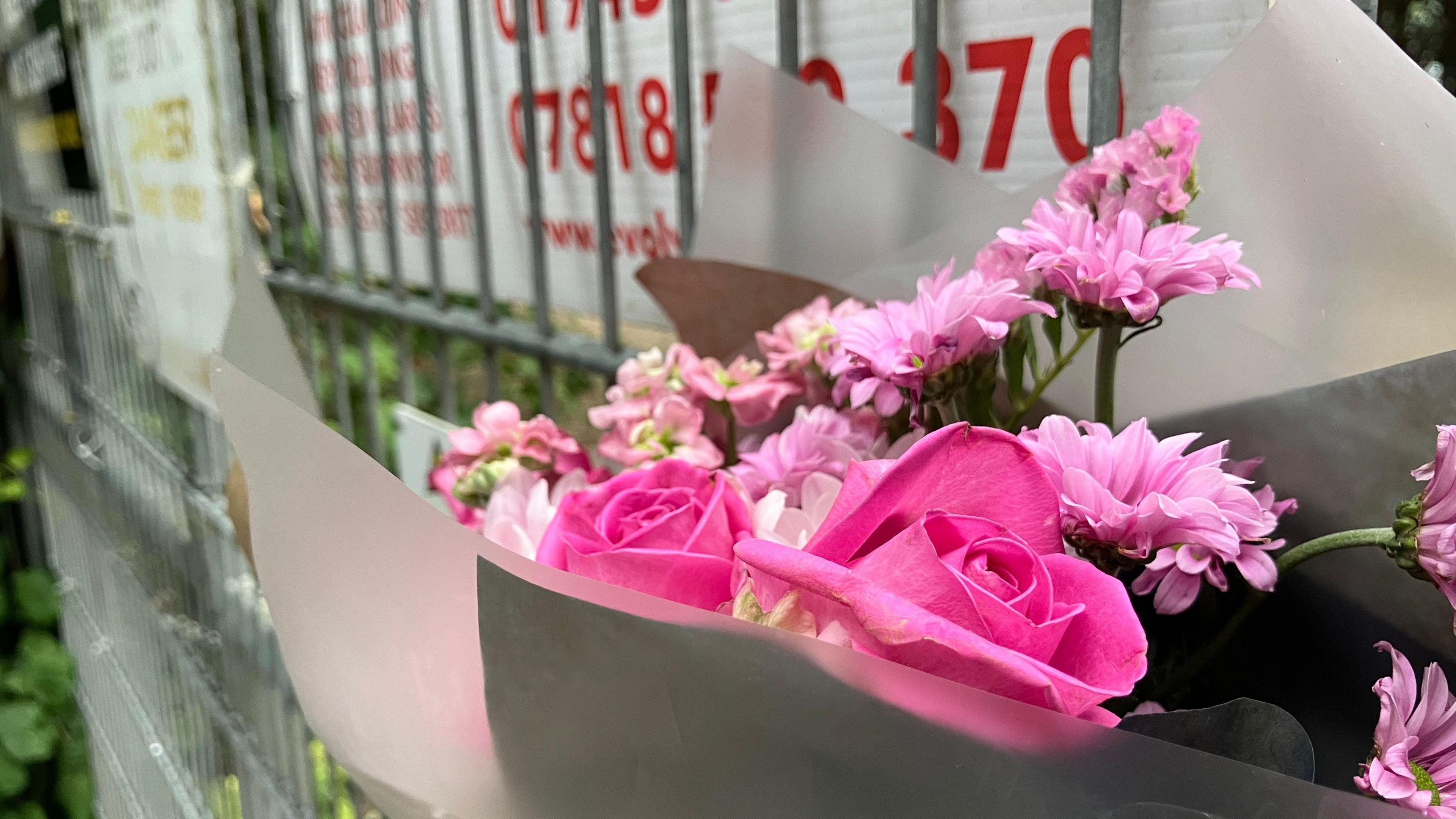 A bouquet of pink flowers strapped to a silver fence. 