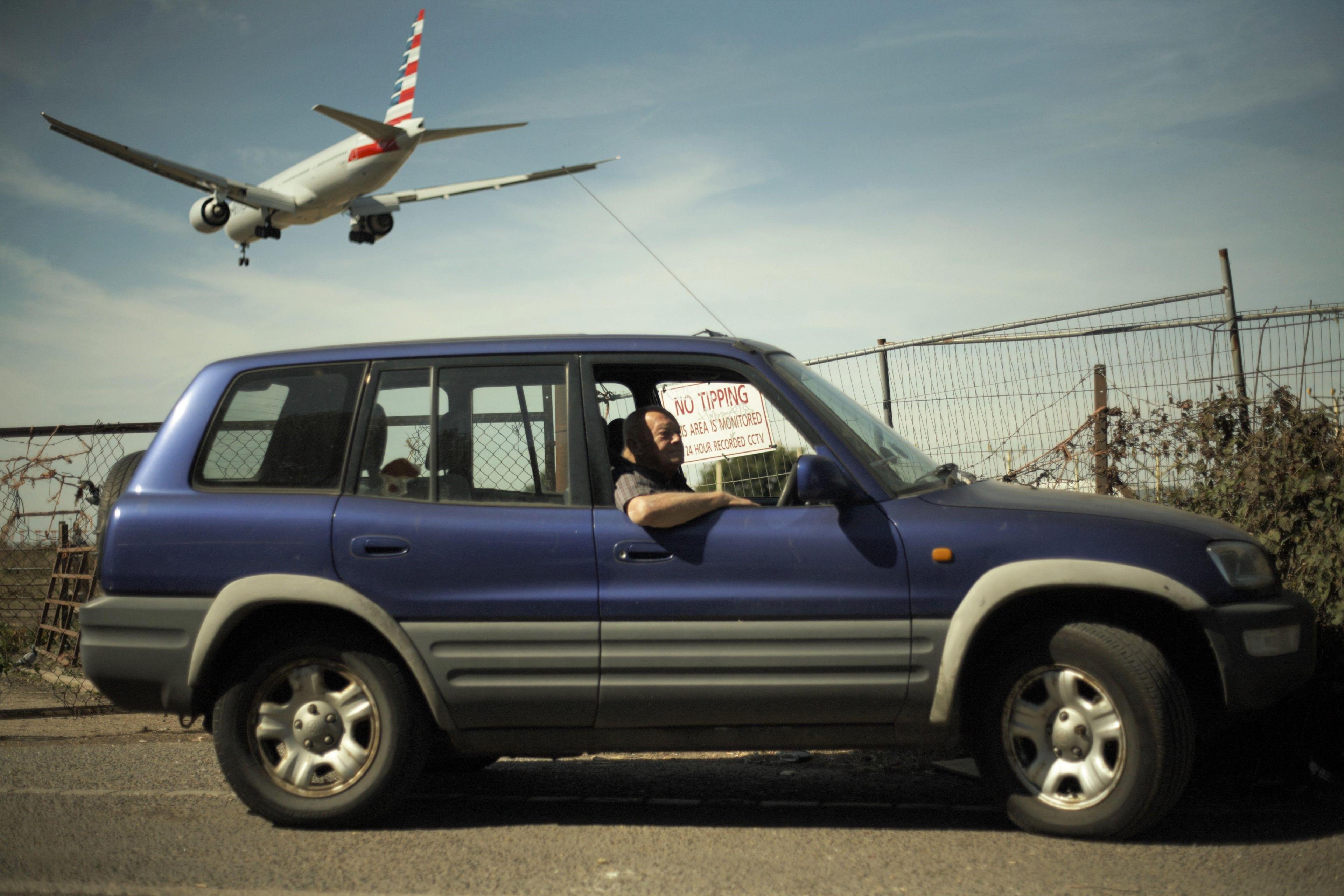 Man in car looks out of the window as a flight passes overhead