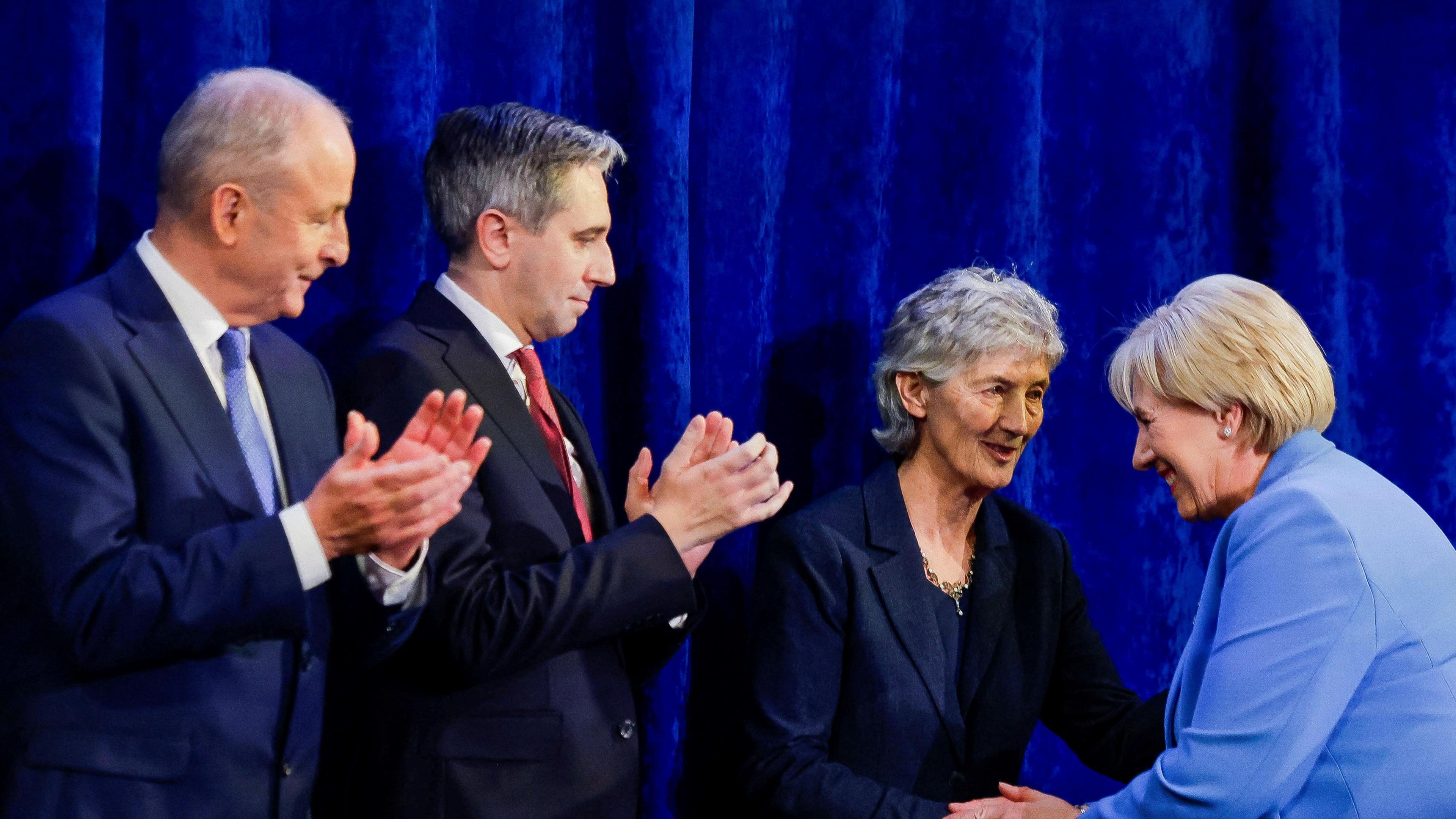 Catherine Connolly shakes hands with Heather Humphreys. They are stood next to Irish Taoiseach Micheal Martin and Irish Tanaiste Simon Harris, who are clapping.