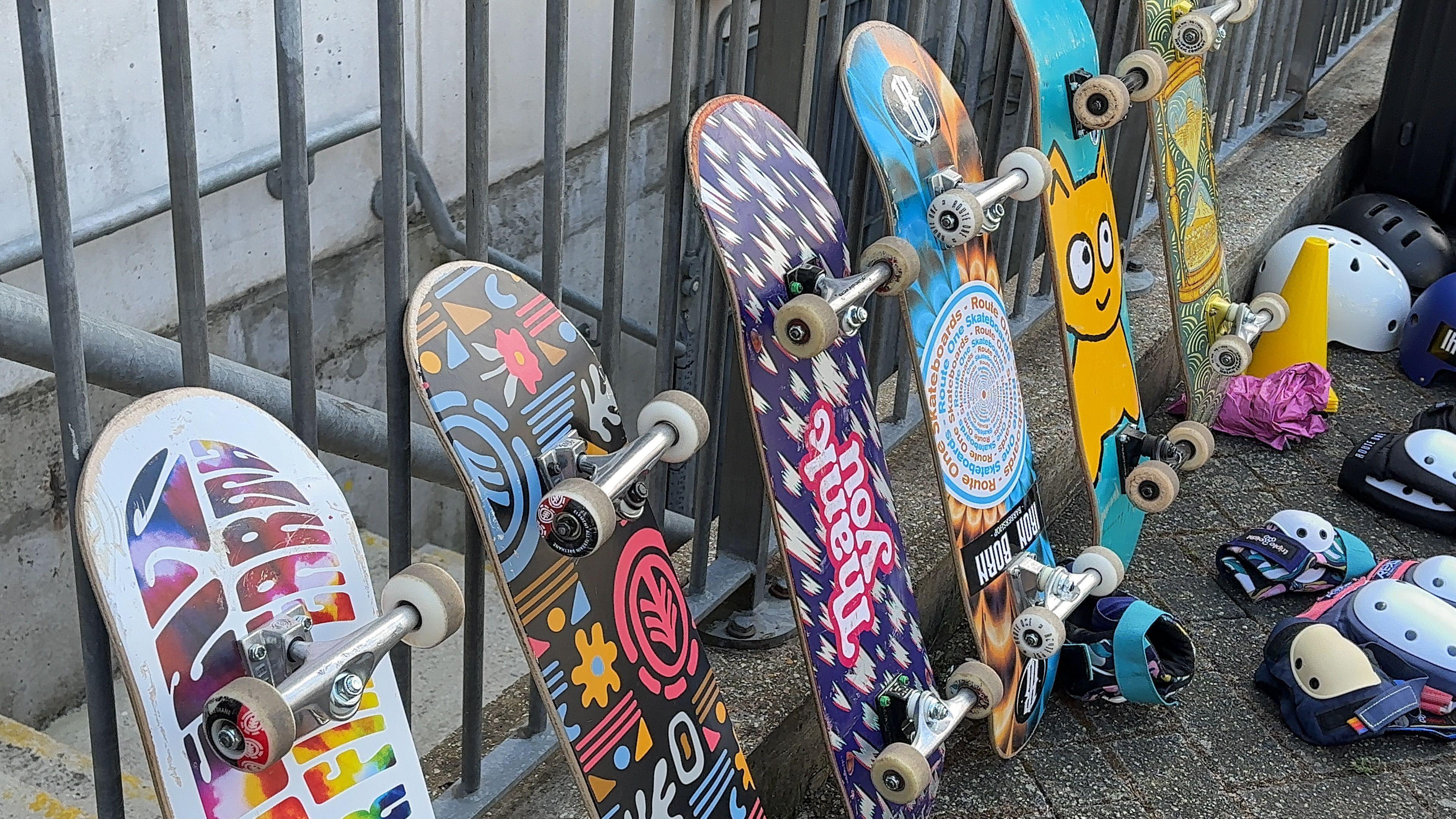 Skateboards lined up against some railings with multiple colours on the base of the decks.