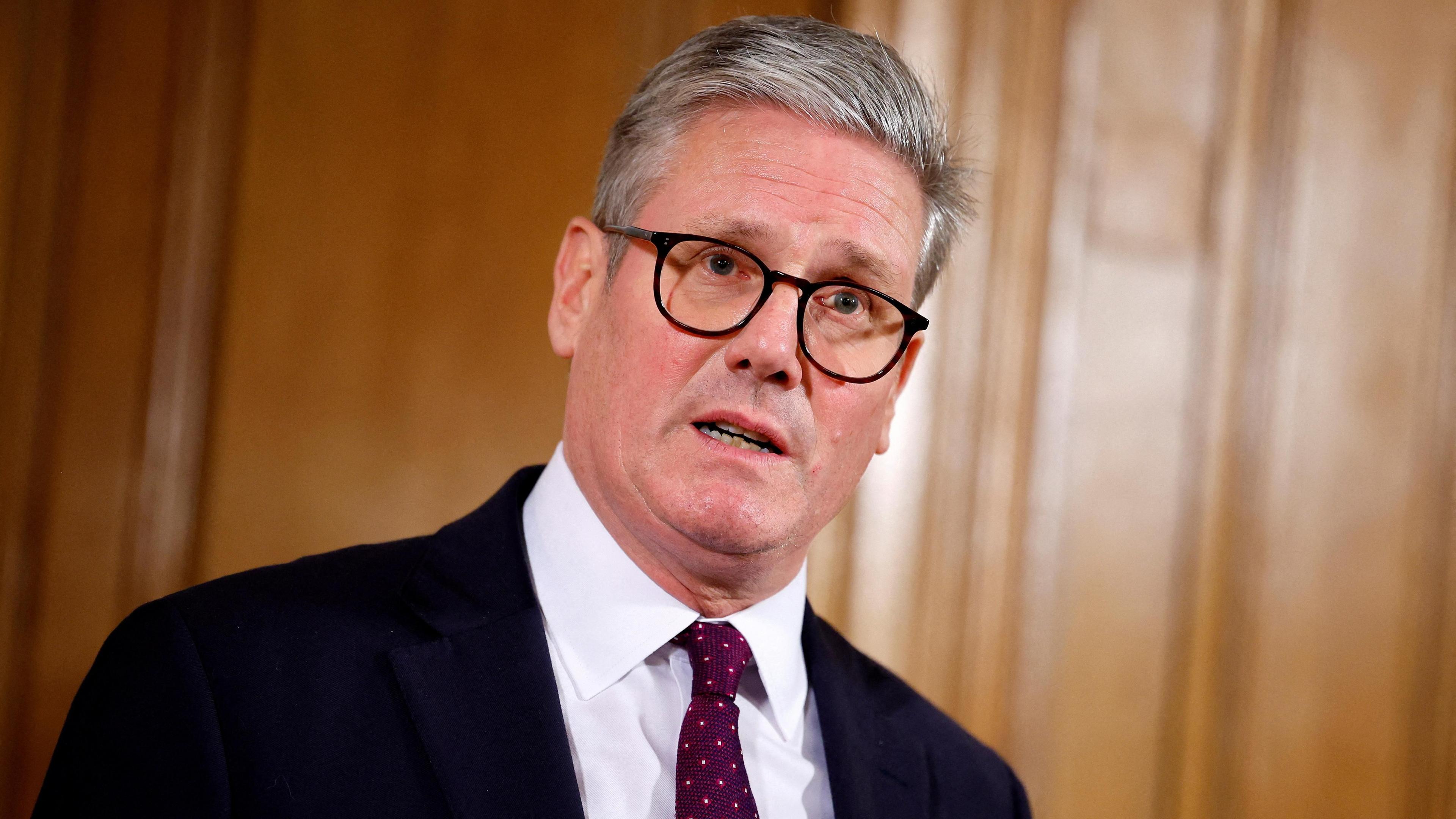 Sir Keir Starmer stands in a wood panelled room inside No 10 wearing a dark blazer, white shirt and patterned red tie.