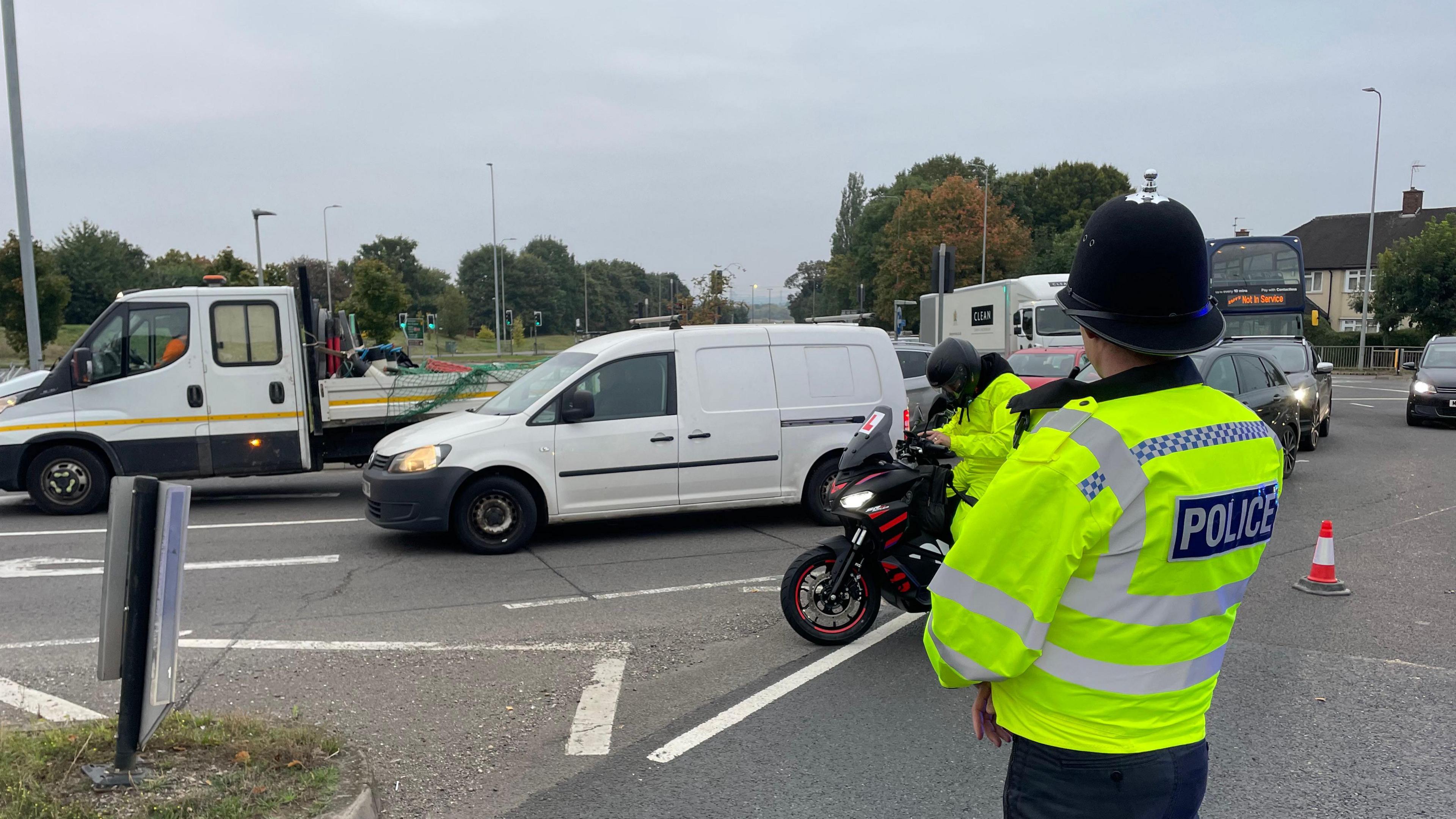 A policeman in high-vis clothing blocks traffic from the A453, and vehicles are seen going around a roundabout instead.